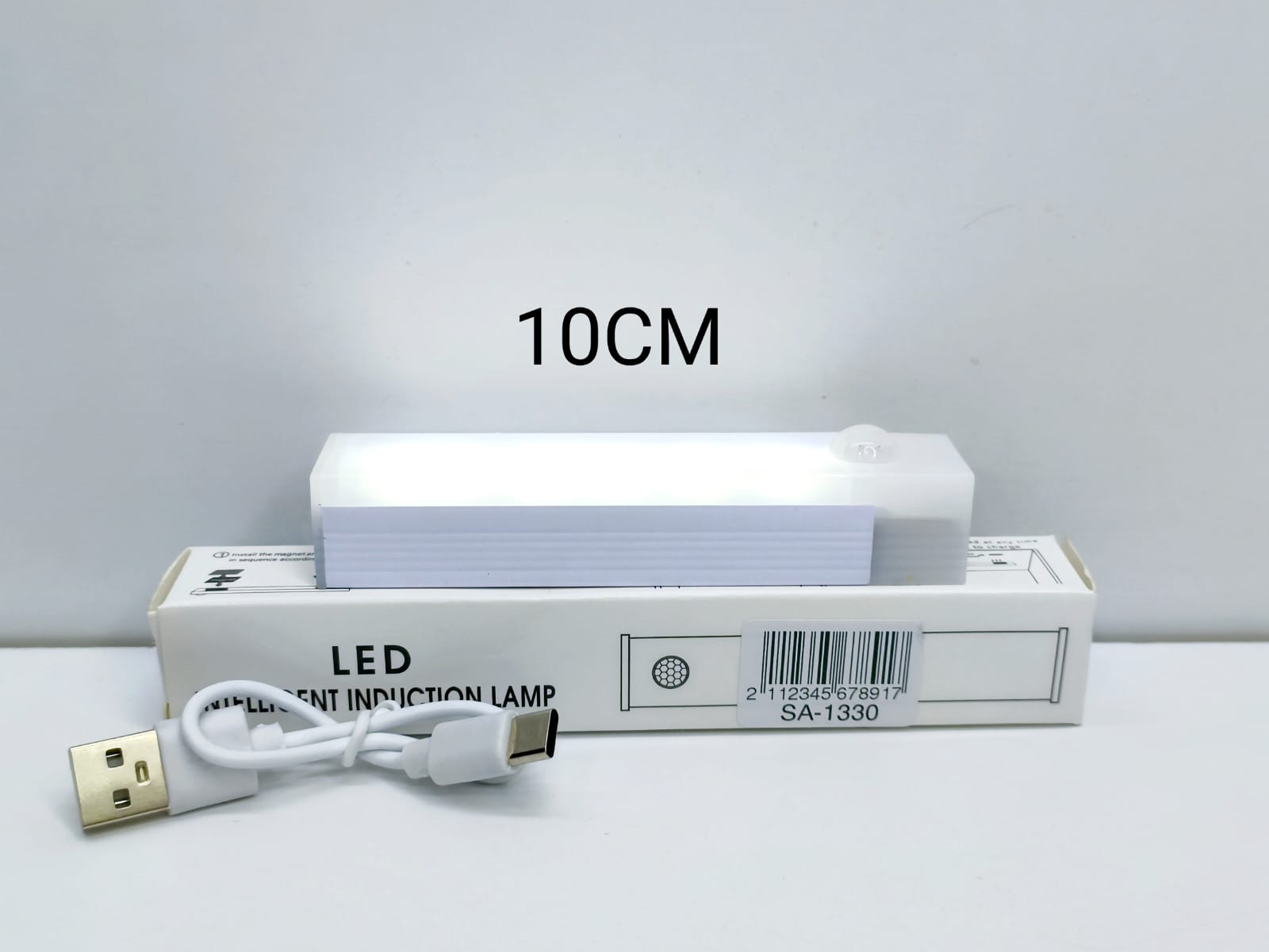 Luz LED recargable con sensor de movimiento de 10 cm encendida, sobre su caja, con el cable USB-C