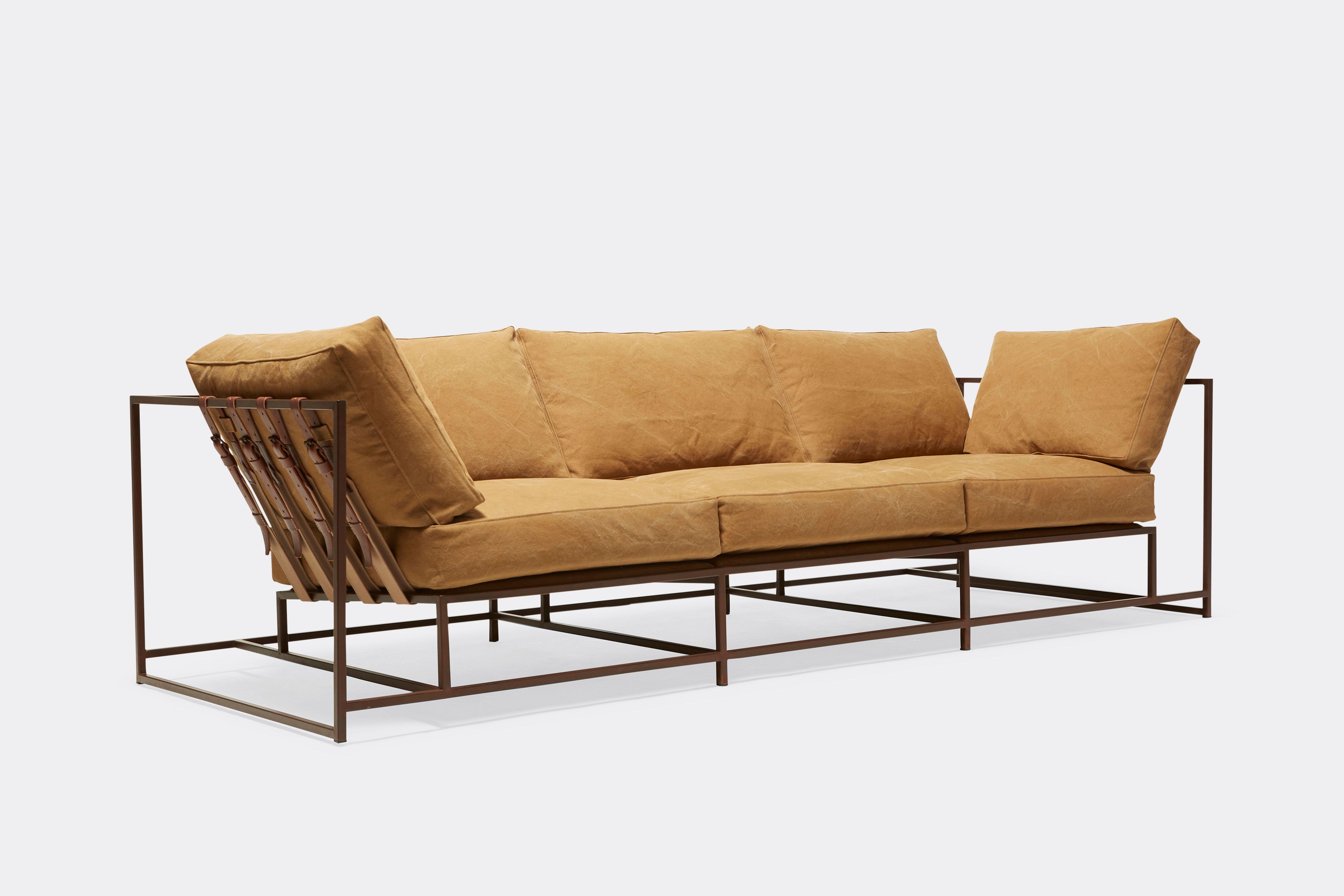 side of sofa with tan canvas upholstery and brown leather belts on marble rust metal frame