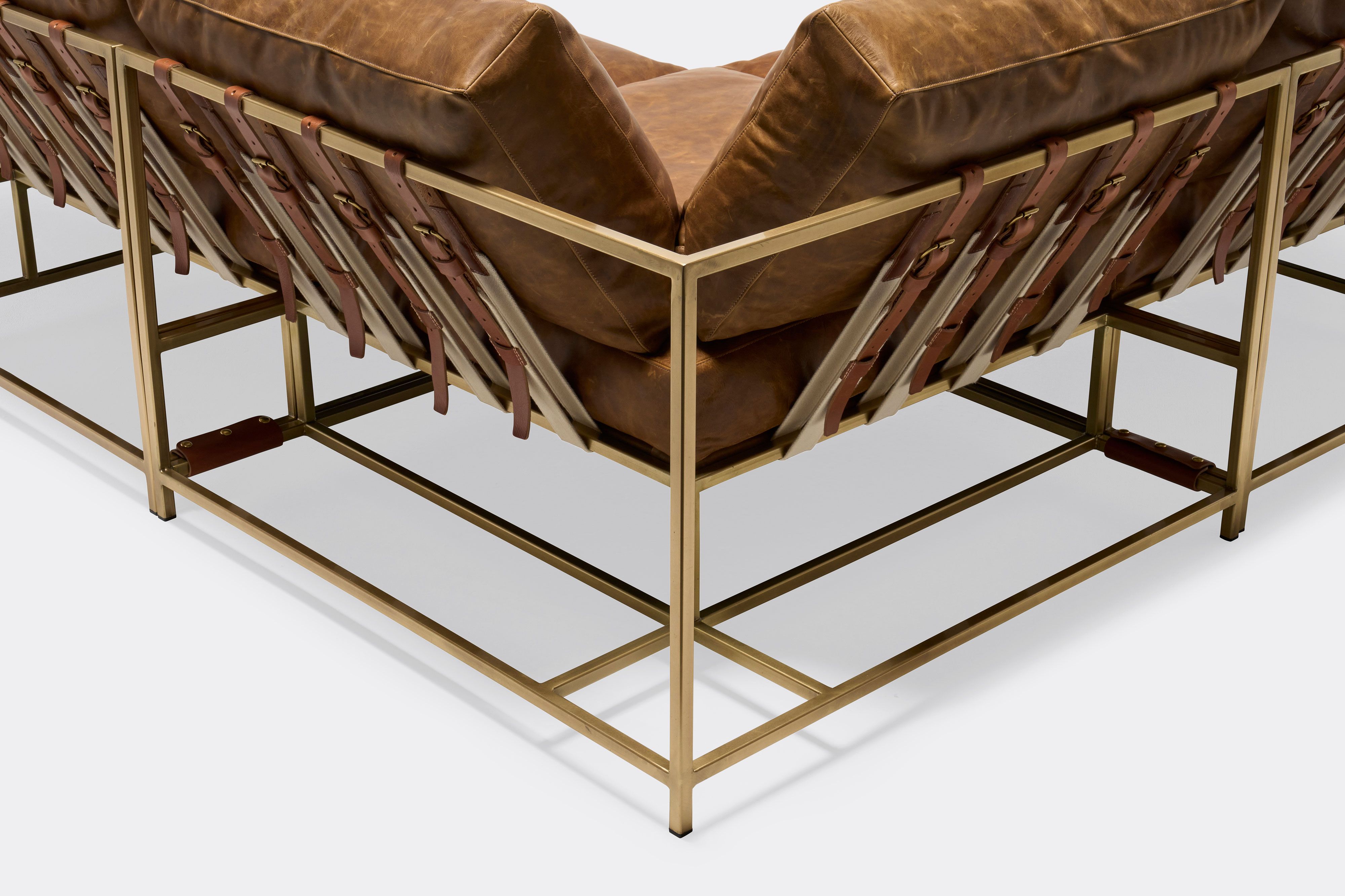 detail of sectional with tan leather upholstery and brown leather belts on antique brass metal frame