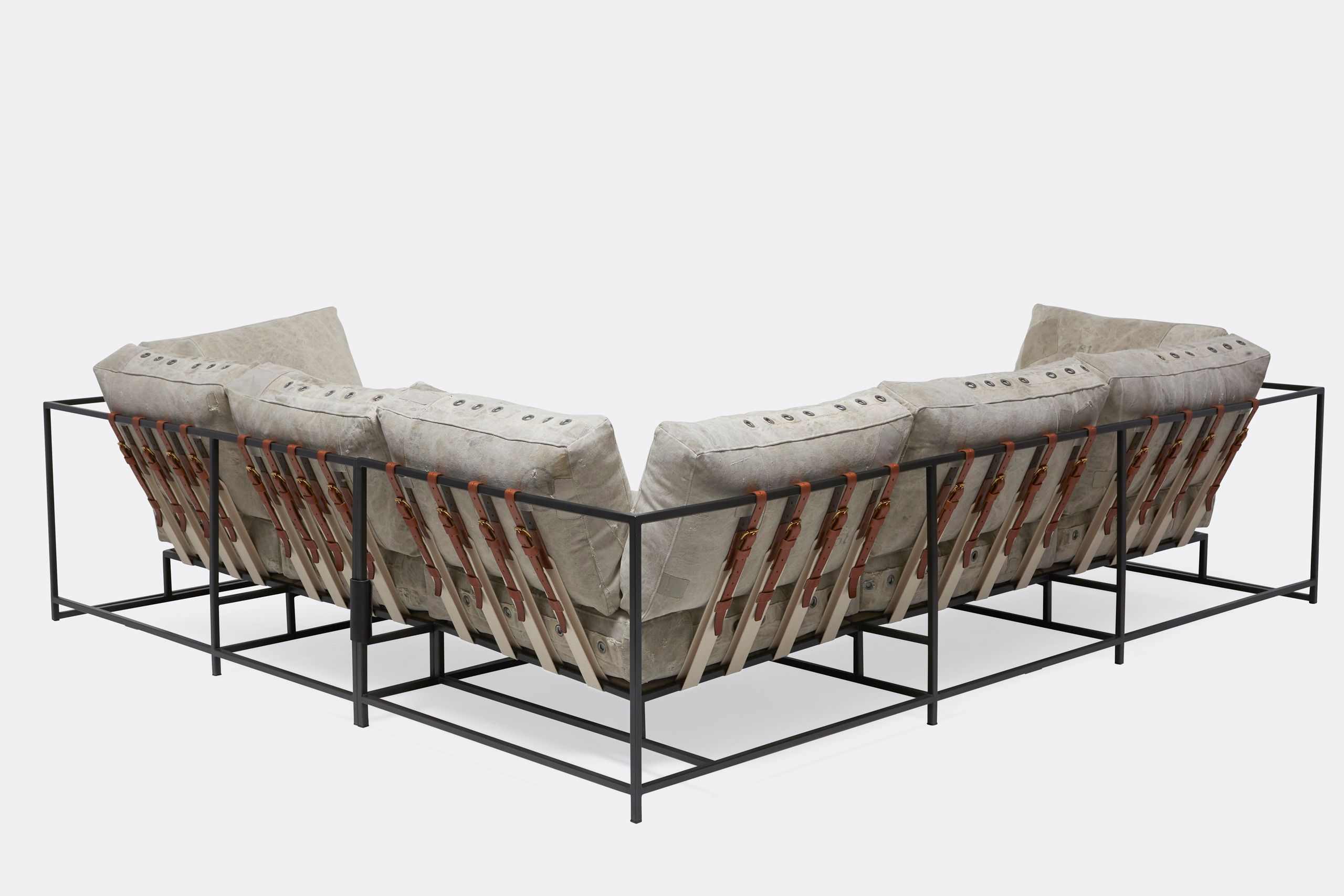 A sofa on with vintage grey canvas covers and leather and webbing straps and on a metal frame shown on a white background