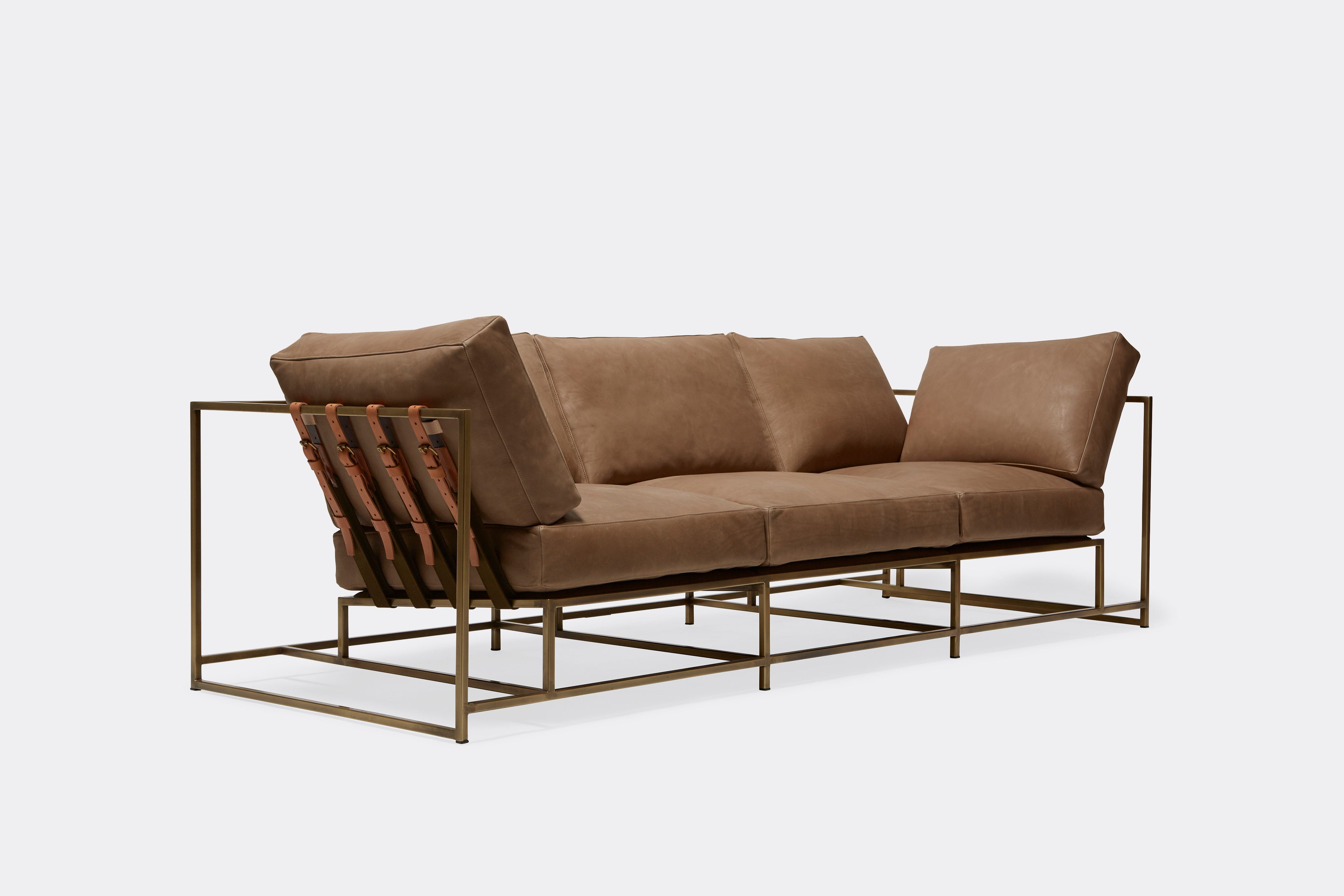 Sideview of Sofa with brown leather upholstery and brown leather belts on antique brass metal frame