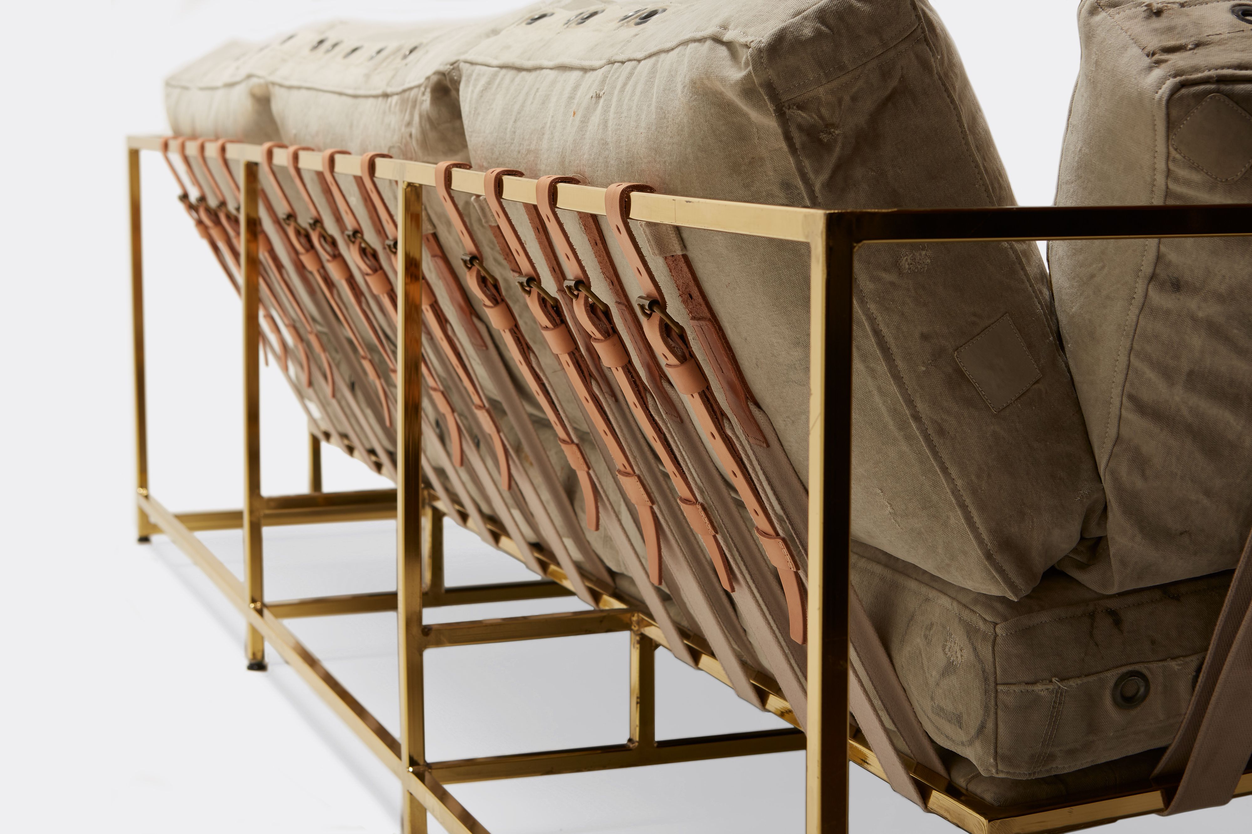 side detail of sofa with grey canvas upholstery and natural leather belts on polished brass metal frame