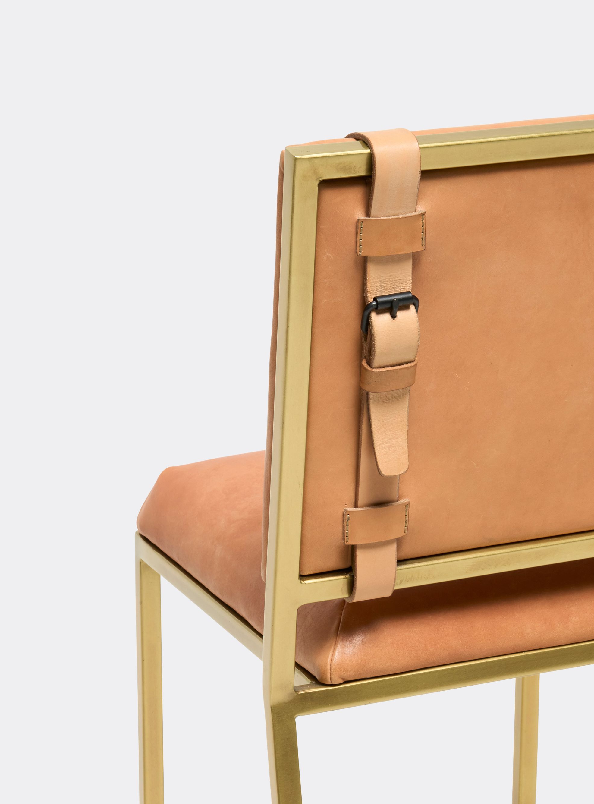 a tan leather barstool with a brass finished steel frame and tan leather belts shown on a white background