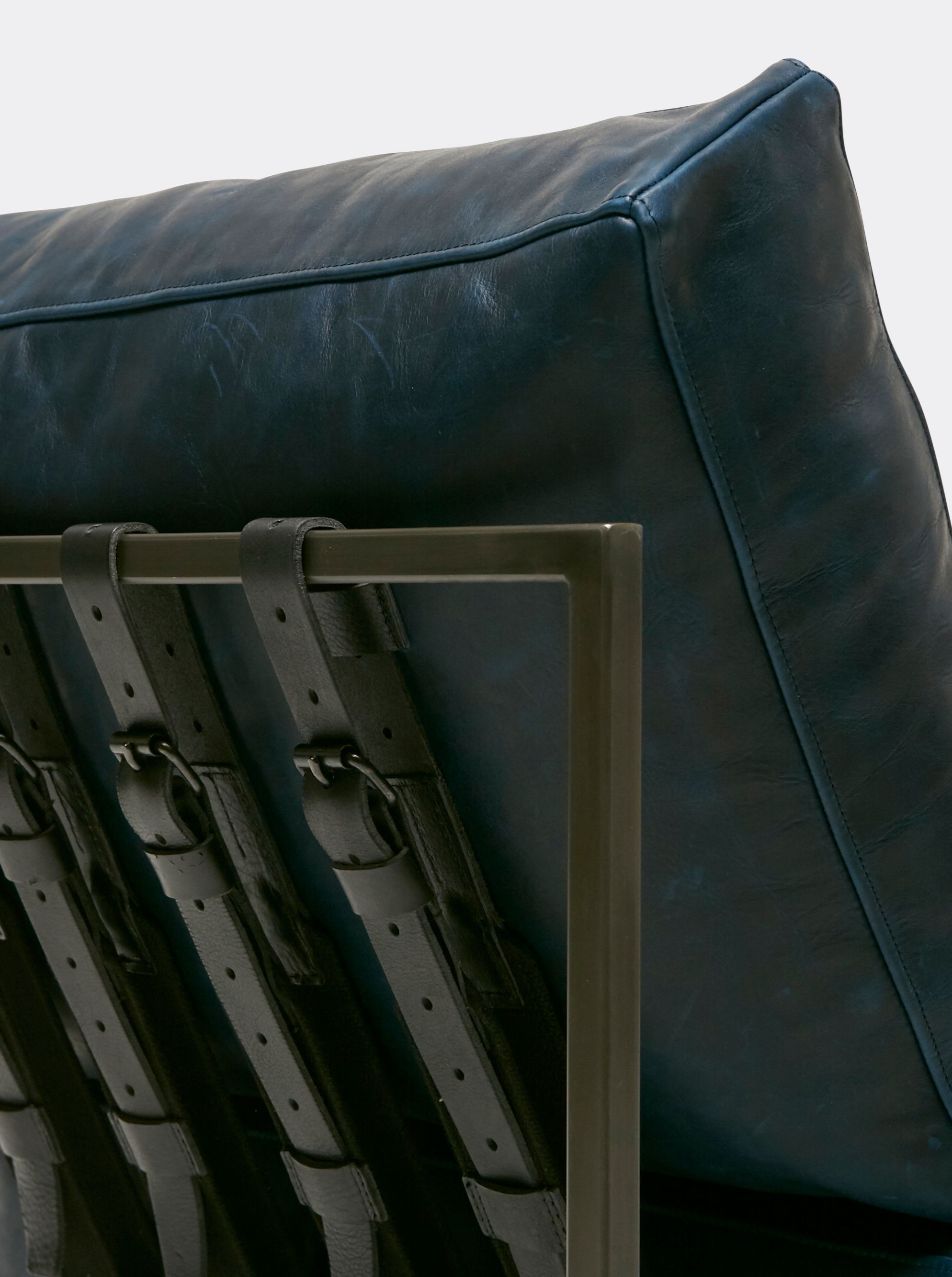 a navy blue leather chair with a black steel frame and black supporting belts shown on a white background .