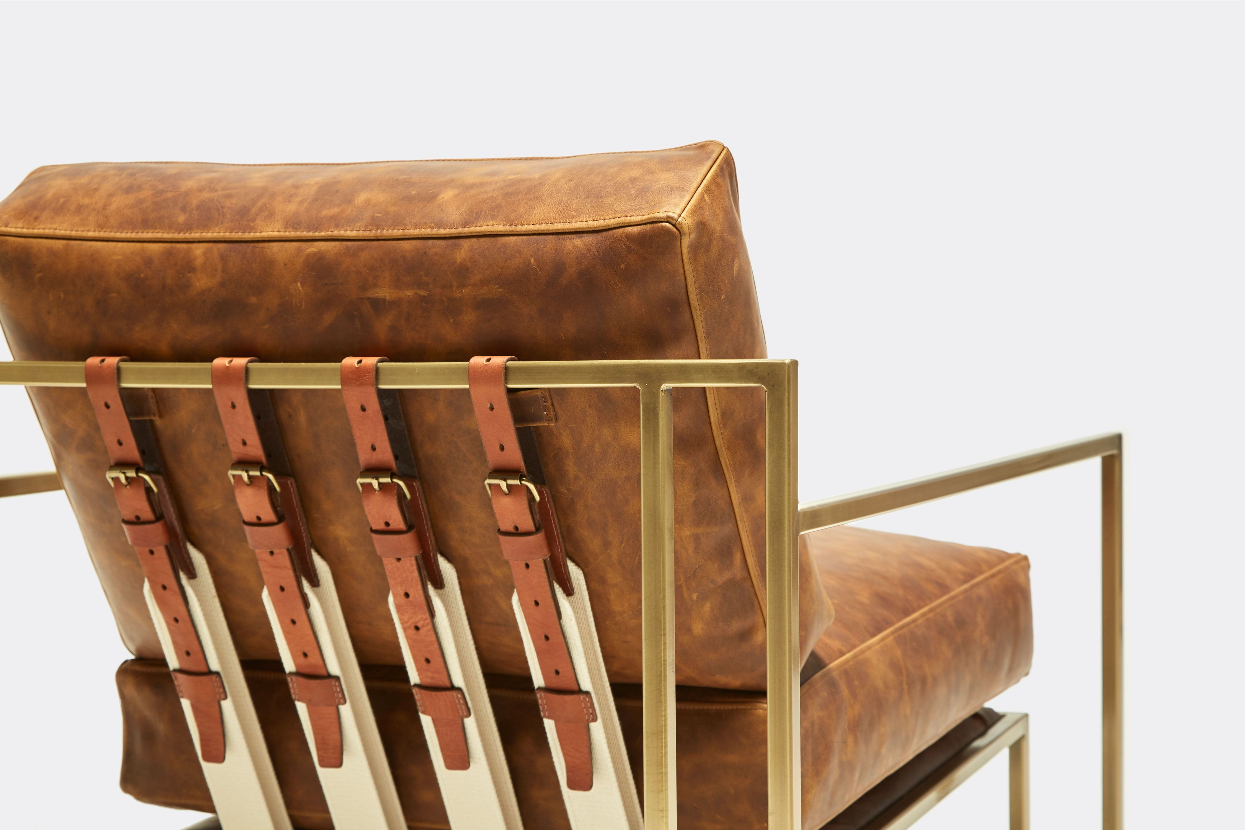 back of armchair with brown leather upholstery and brown leather belts on antique brass metal frame