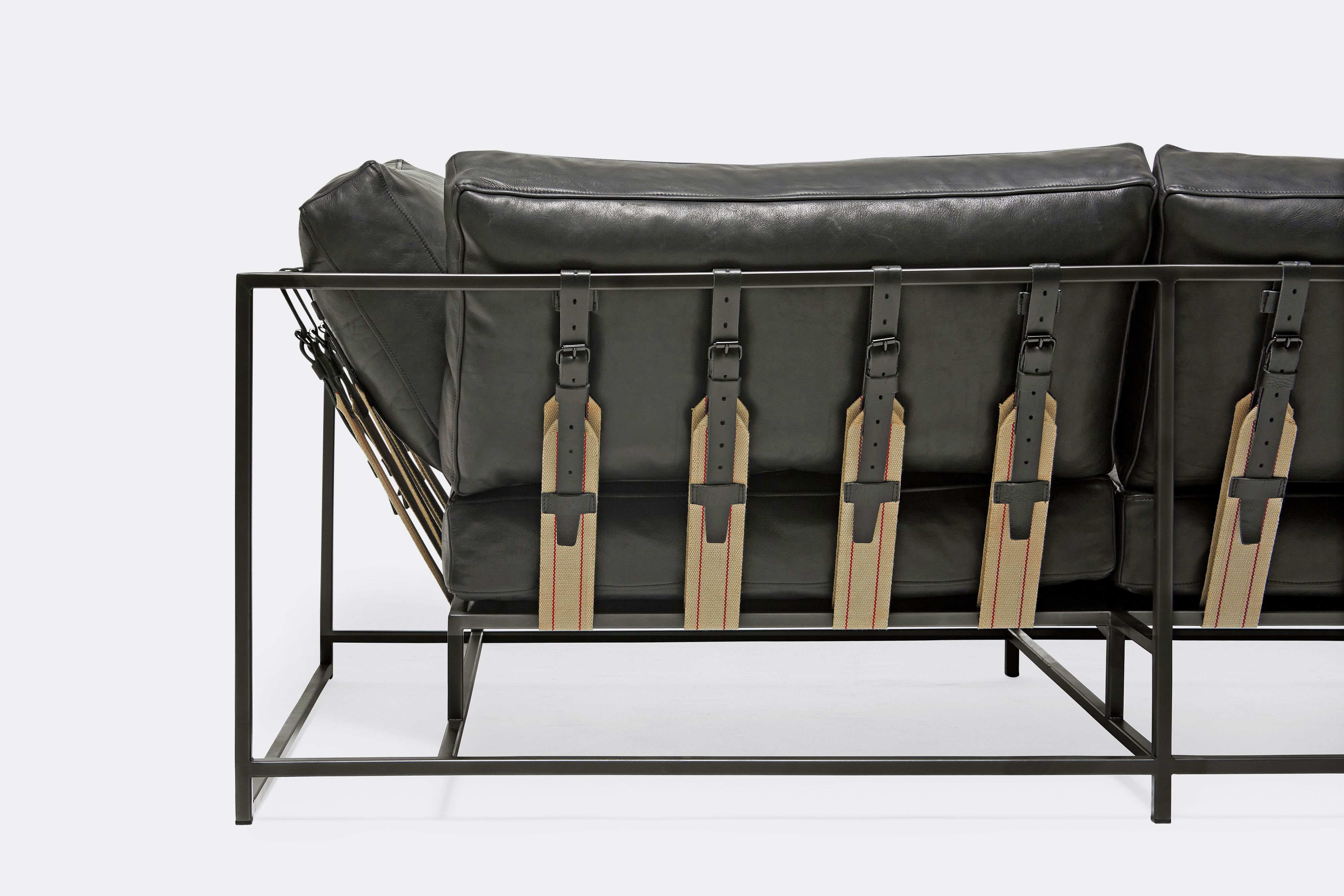 back detail of two seat sofa black leather upholstery and black leather belts on black metal frame