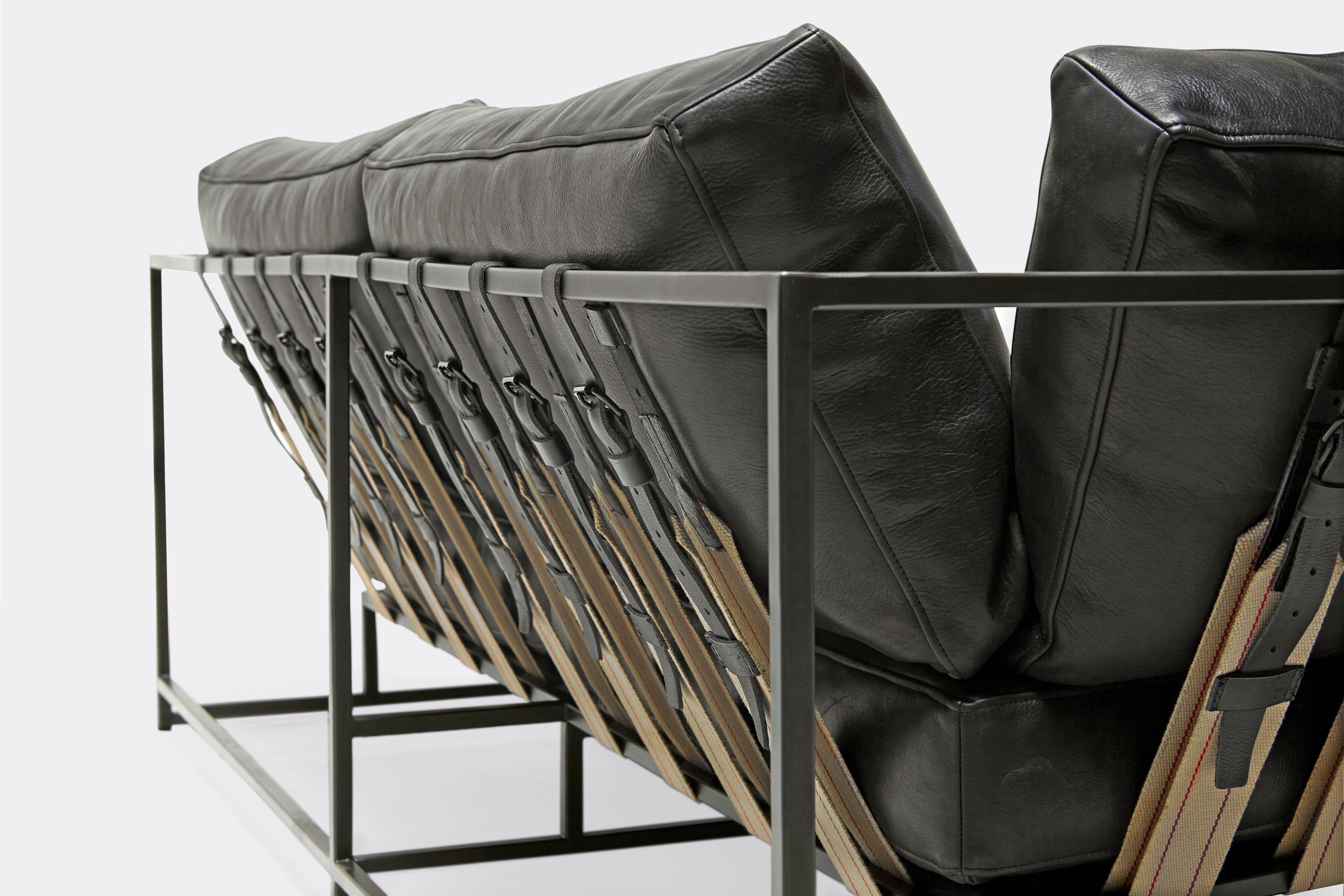back detail of two seat sofa black leather upholstery and black leather belts on black metal frame