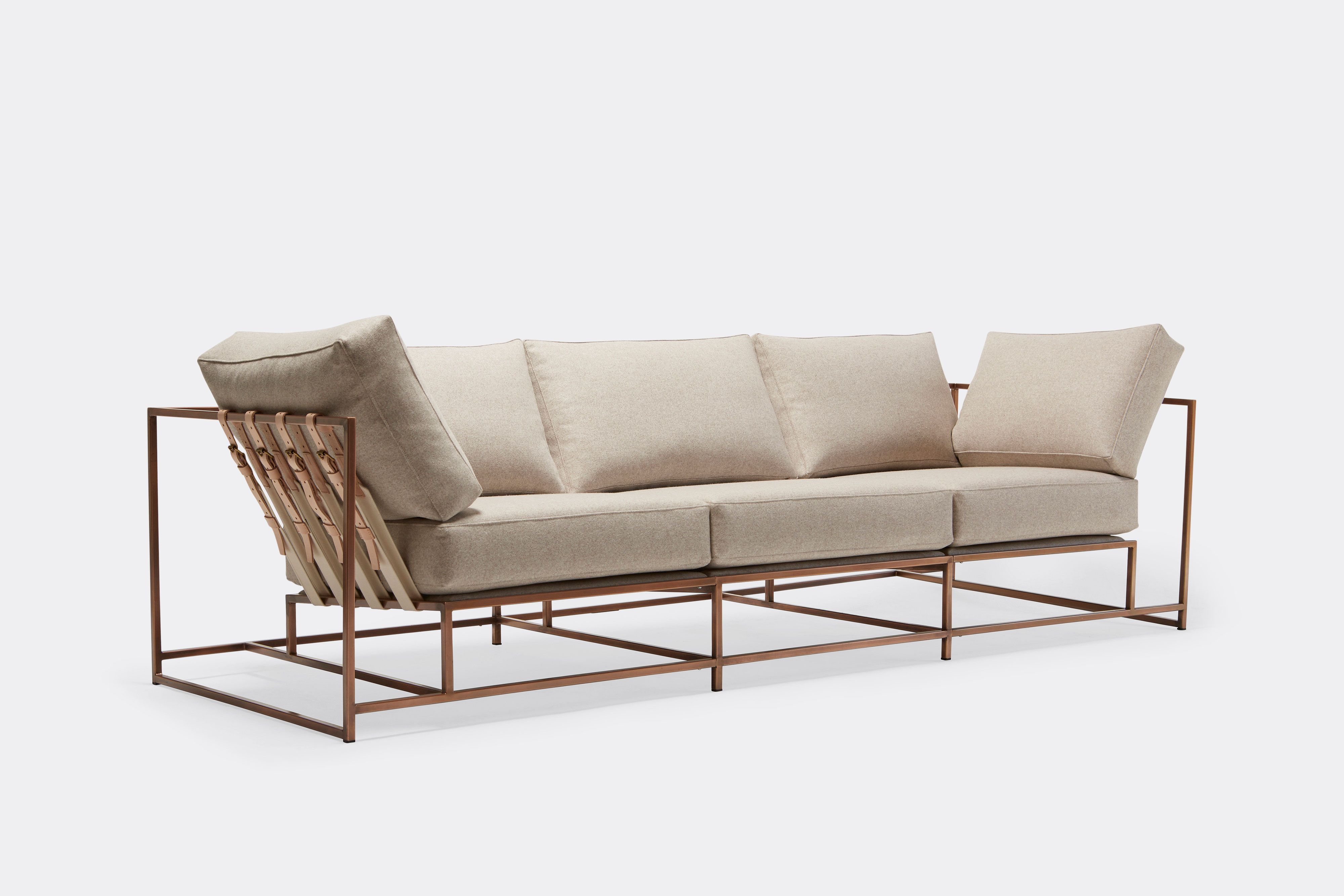 side of three piece sofa with cream wool upholstery and natural tan leather belts on antique copper metal frame