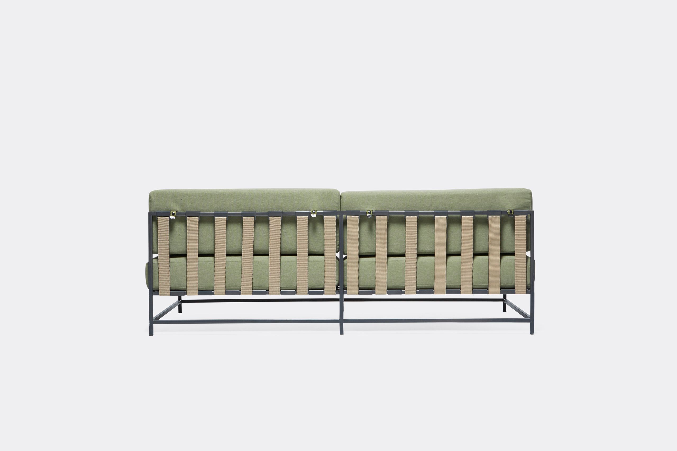 a steel framed sofa with black metal finish and green cushions and supporting belts on a white background .