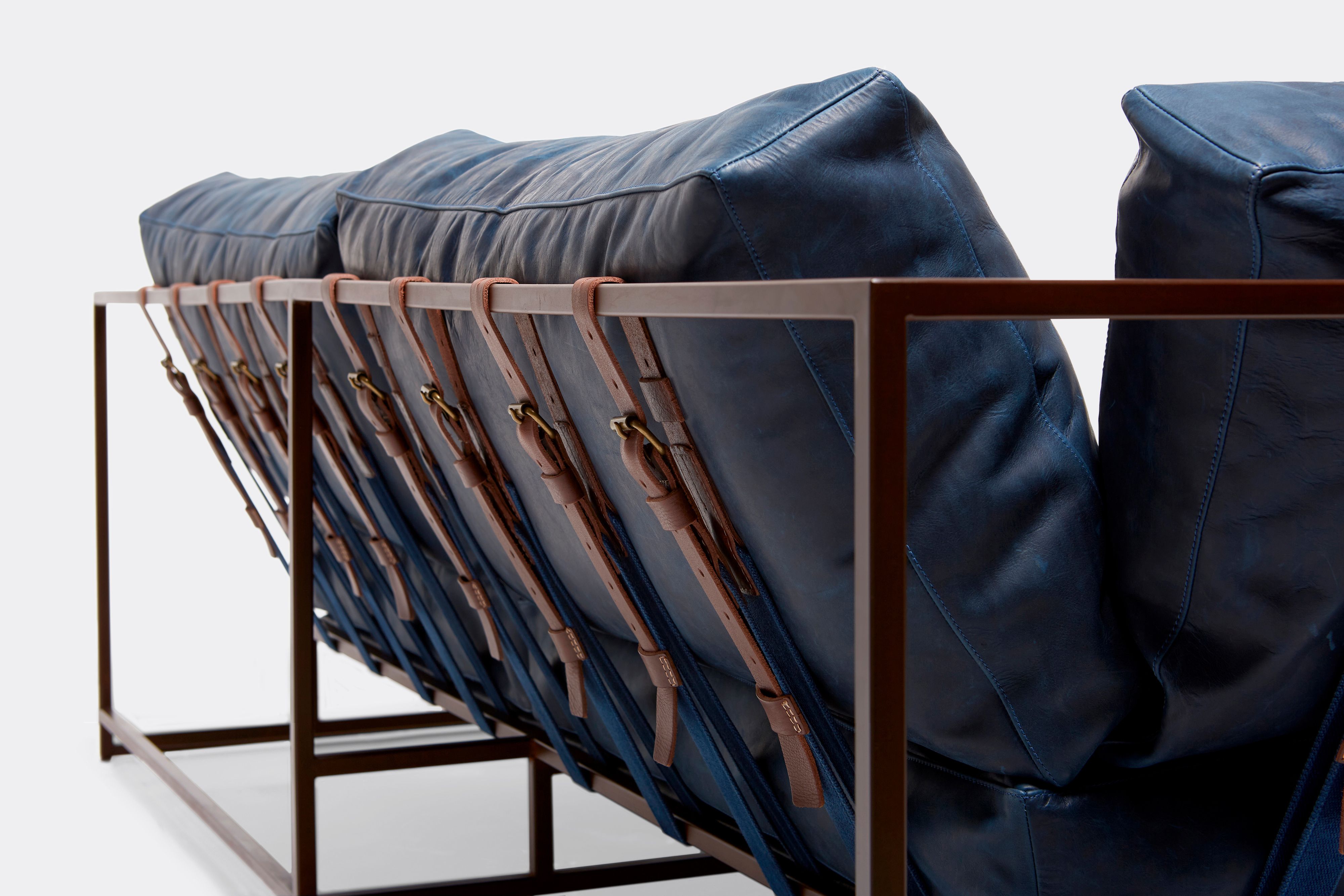 back of two seat sofa with blue leather upholstery and brown leather belts on marble rust metal frame