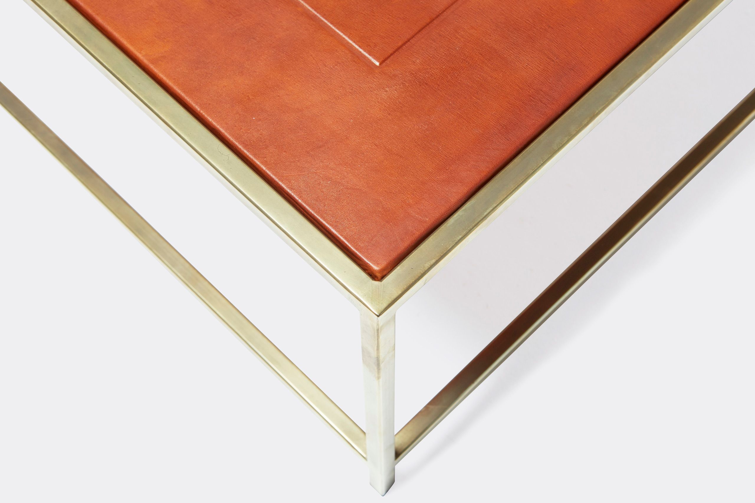 a square coffee table with a leather top and a brass frame on a white background .