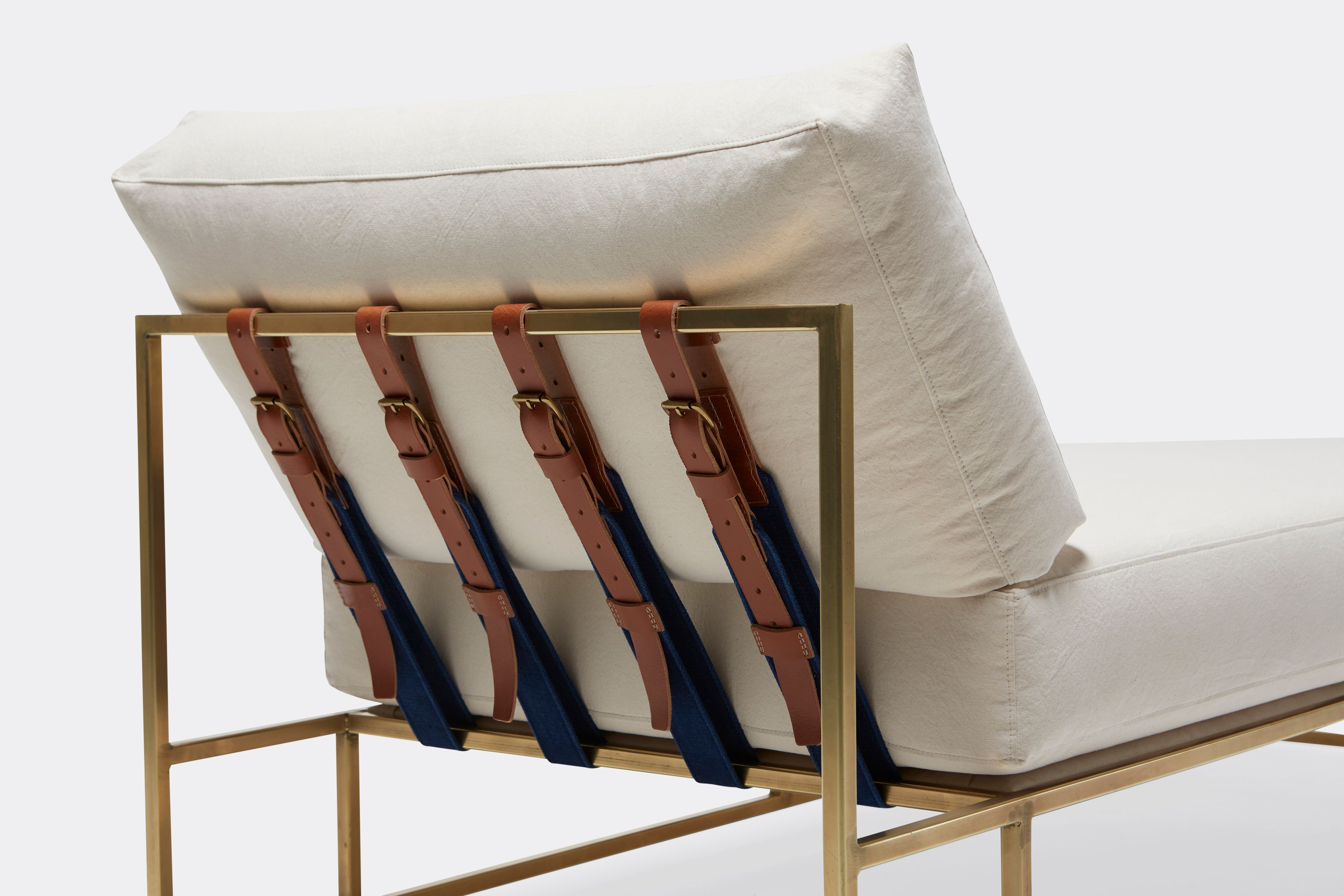 Detail of lounge chaise with natural canvas upholstery and brown leather belt on tarnished brass metal frame