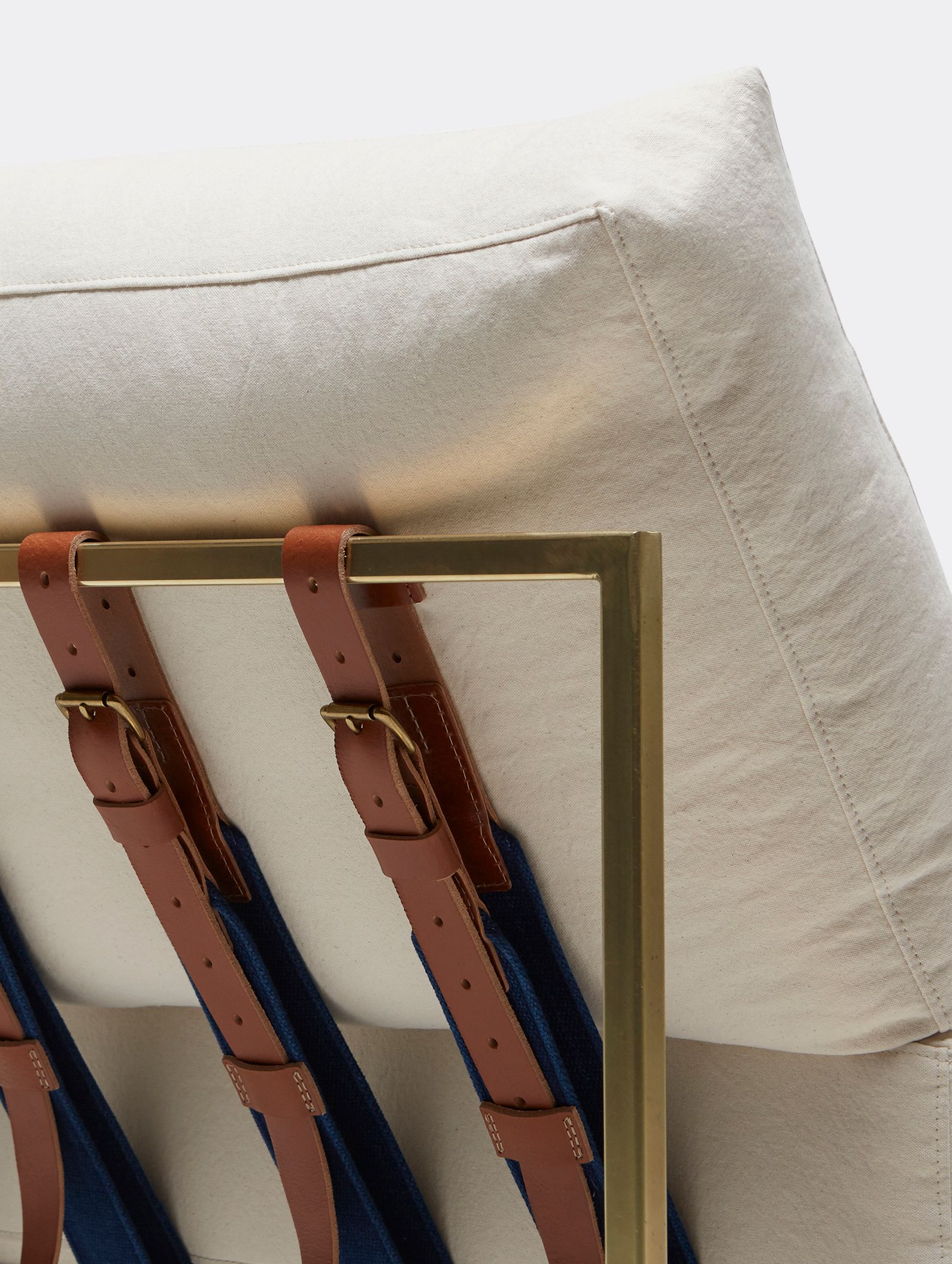 Natural canvas upholstered chaise lounge on antique brass finished frame with leather and webbing supporting belts shown on a white background