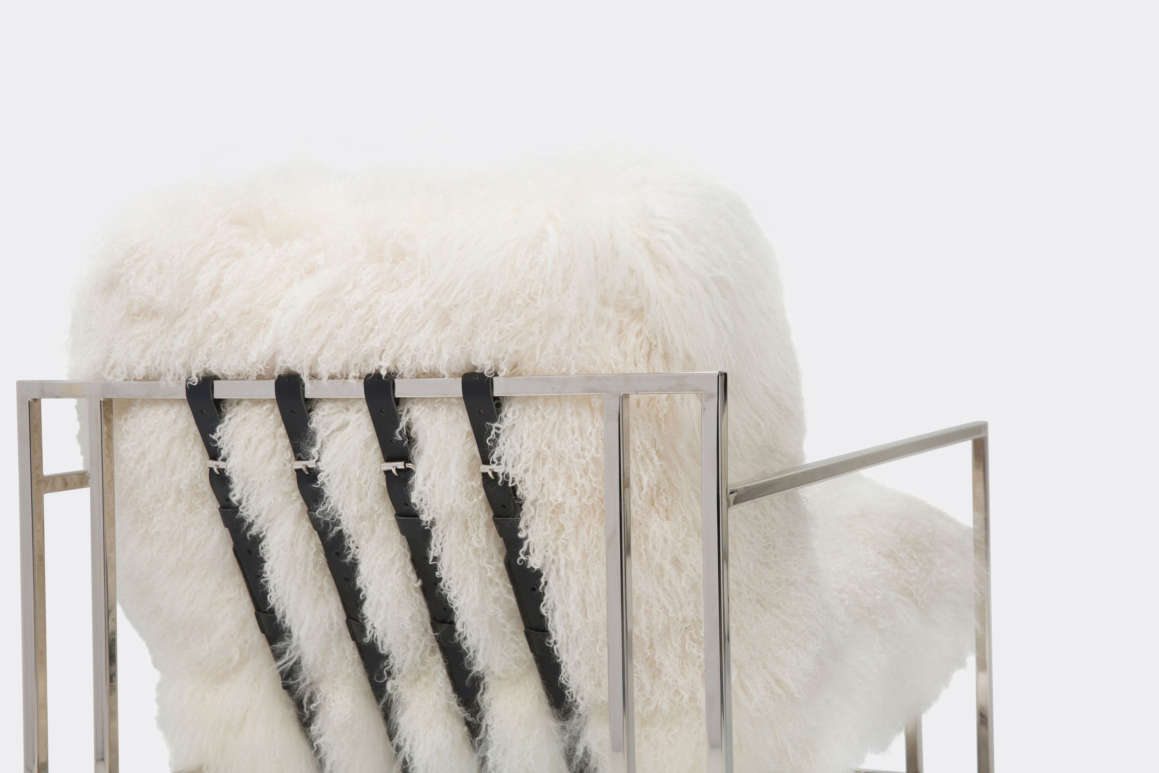 back of armchair with white sheepskin upholstery and black leather belts on polished nickel metal frame