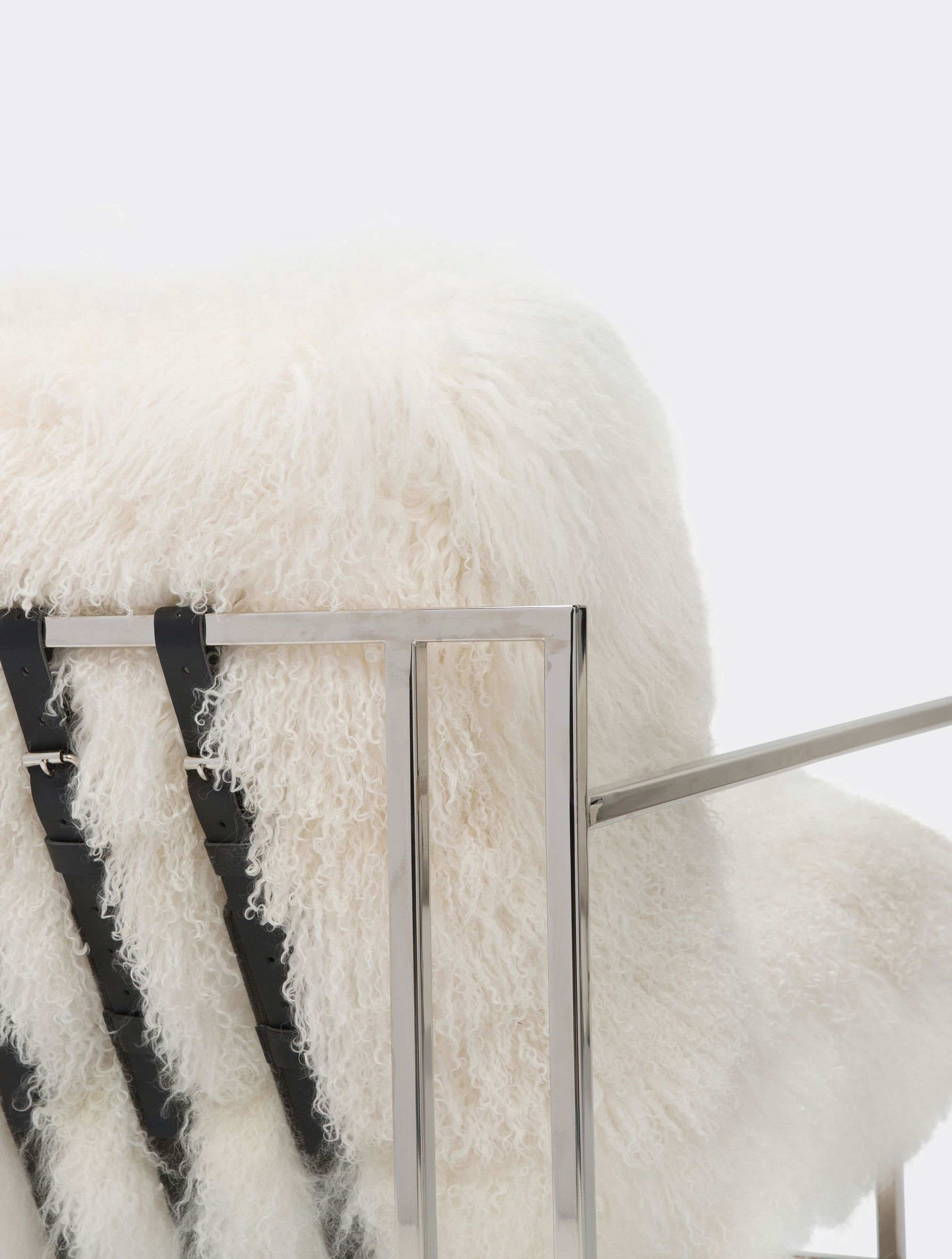 a white sheepskin armchair with black supporting belts on the back is sitting on a white surface .