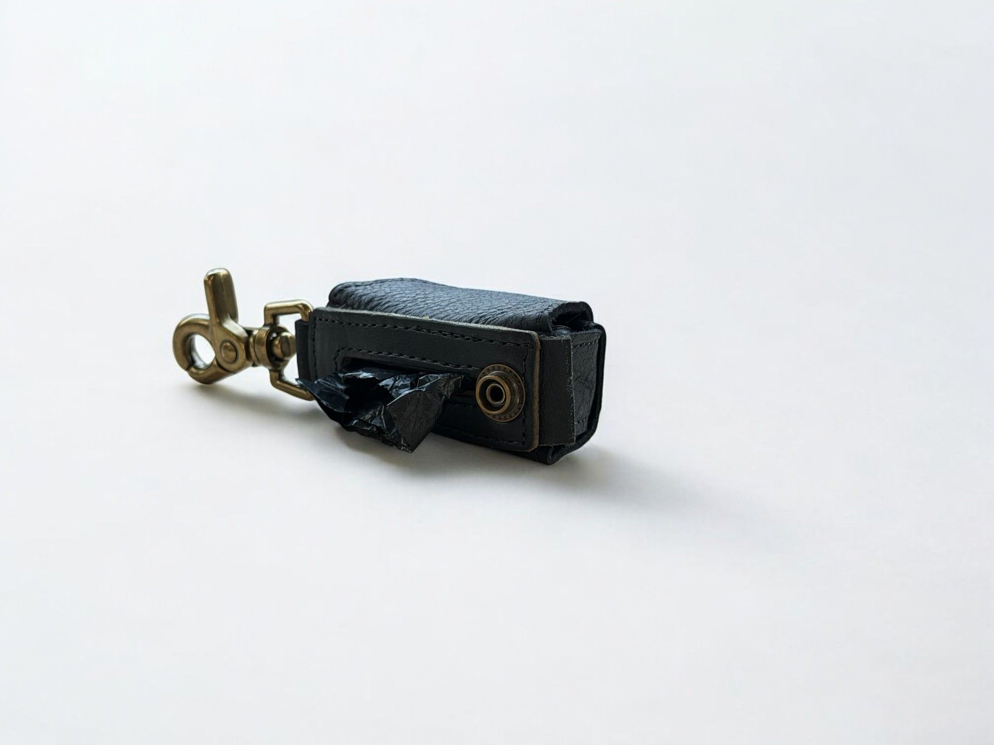 Black leather pet waste bag dispenser with a brass clip, showing a black bag emerging.