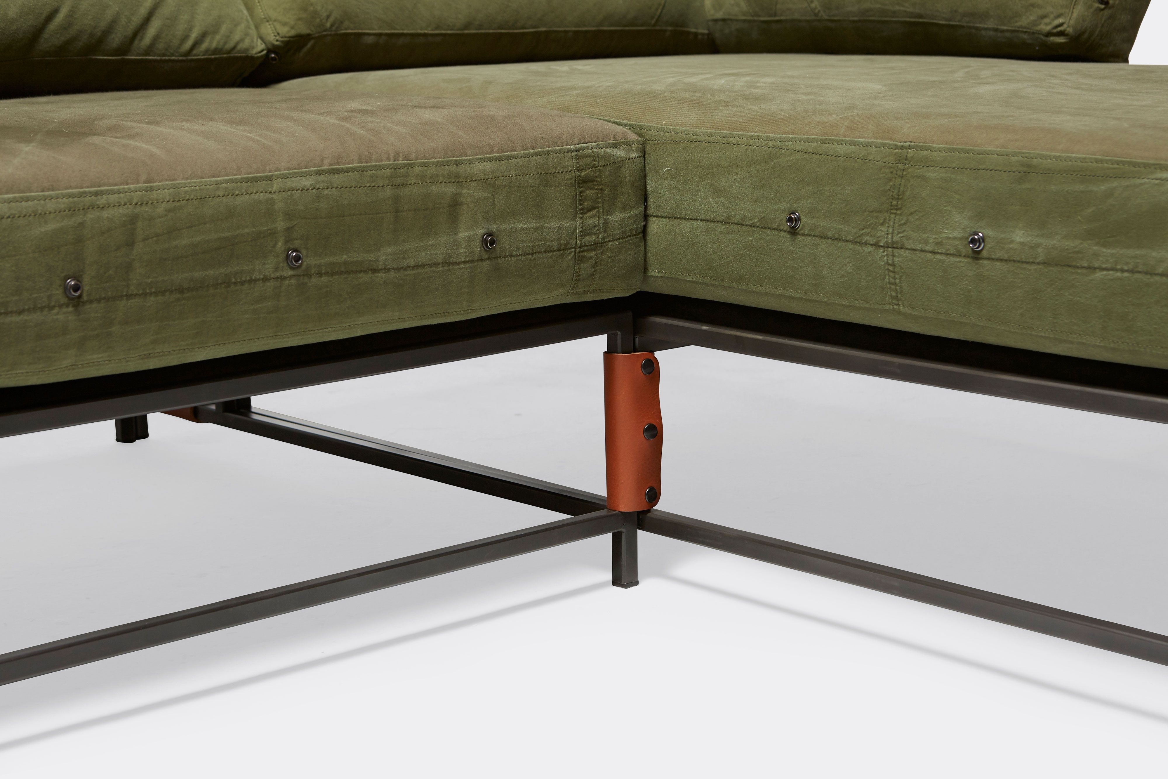 detail of sectional with green canvas upholstery and brown leather belts on black metal frame