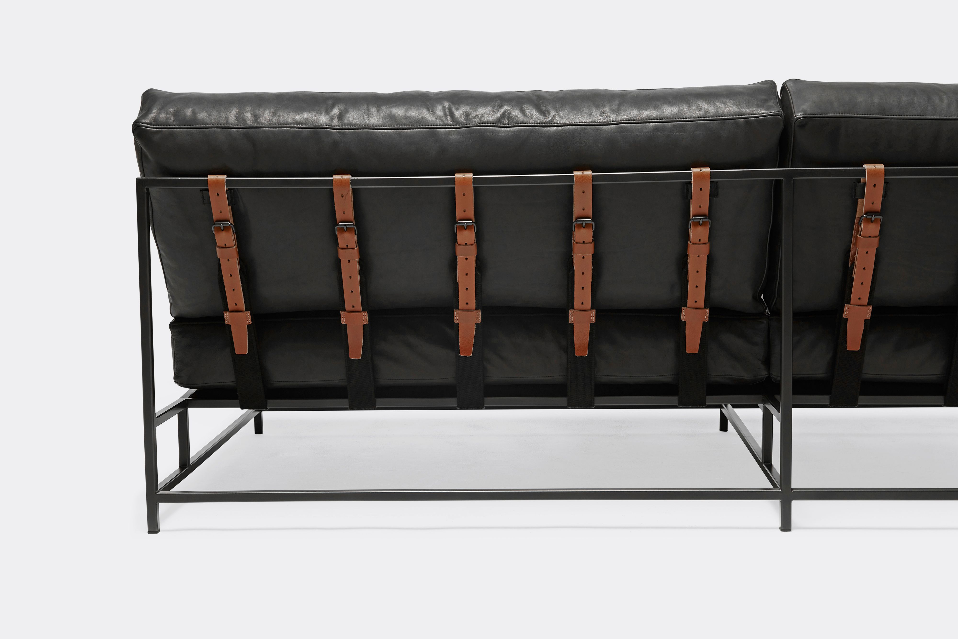 back of loveseat with black leather upholstery and brown leather belts on black metal frame