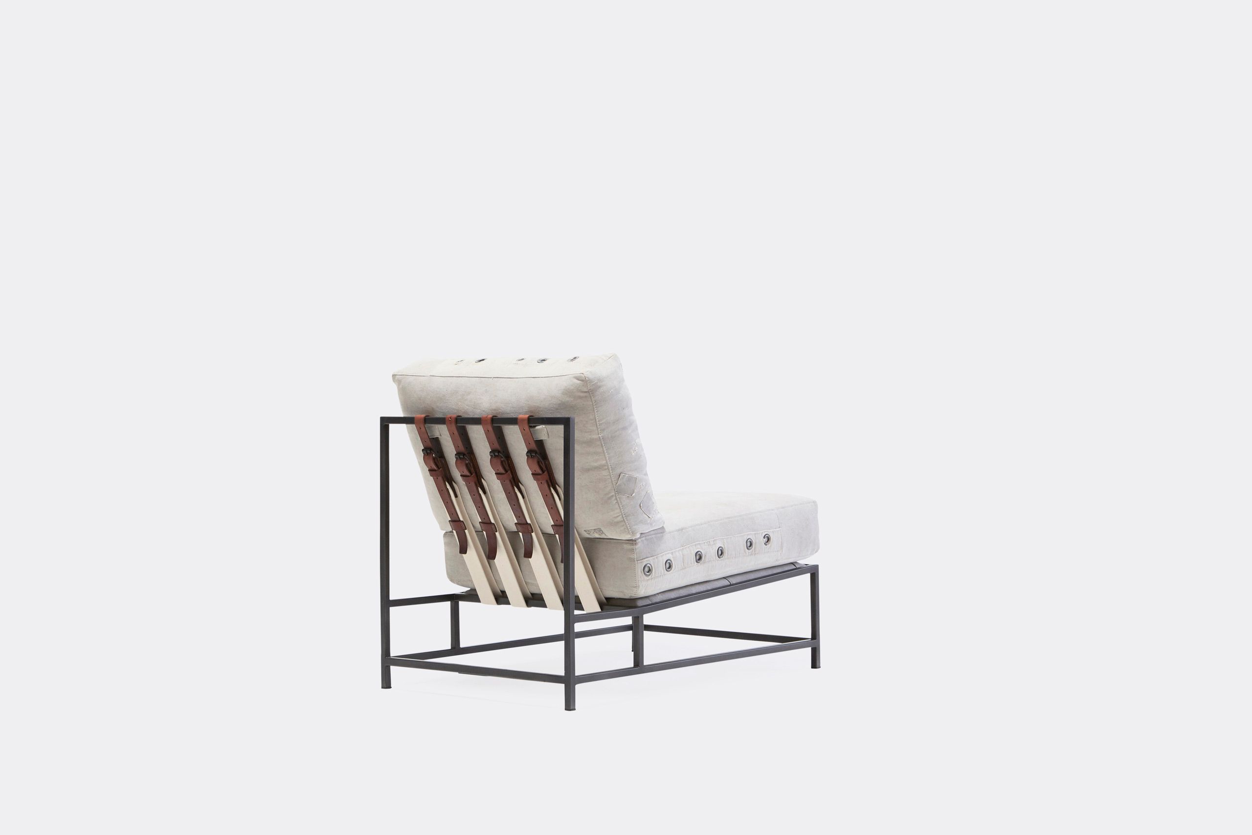 A chair with a white cushion and leather straps atop a blackened steel frame on a white background