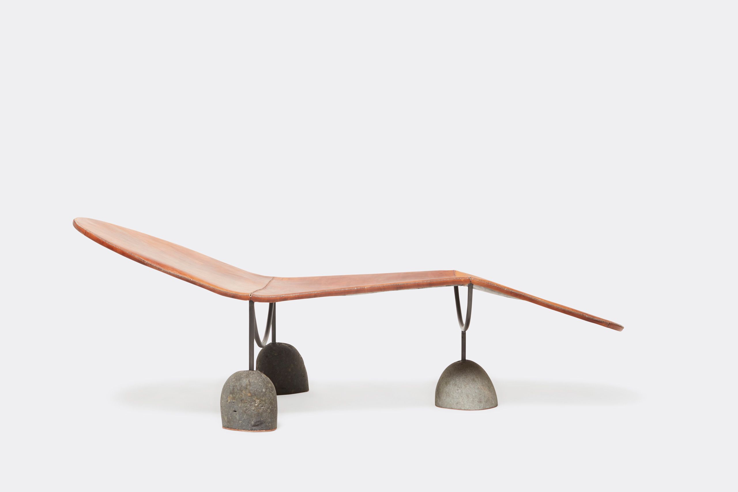 a brown leather chaise lounge with a steel frame and stone base shown on a white background .