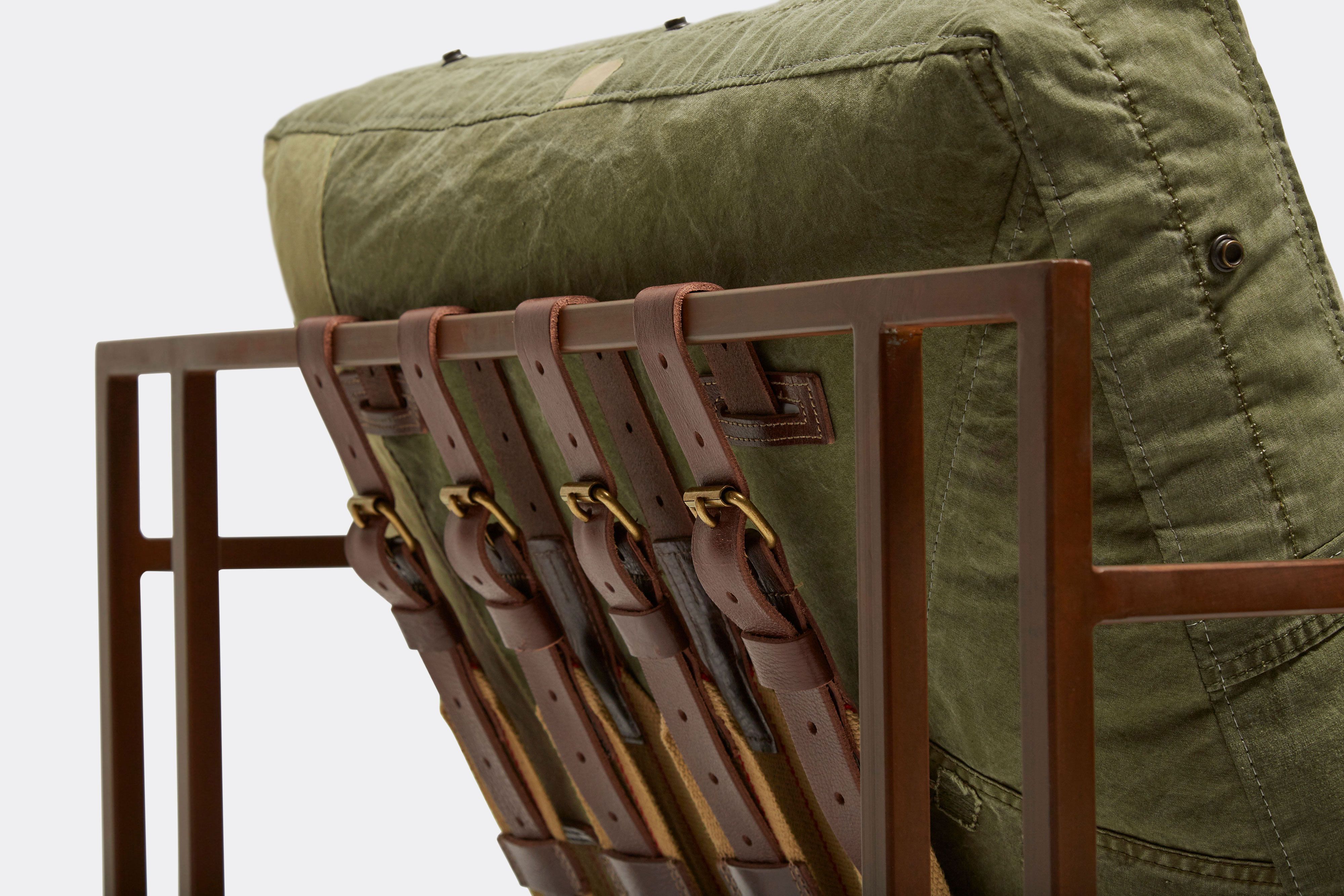a steel framed chair with a green cushion and supporting belts on a white background .