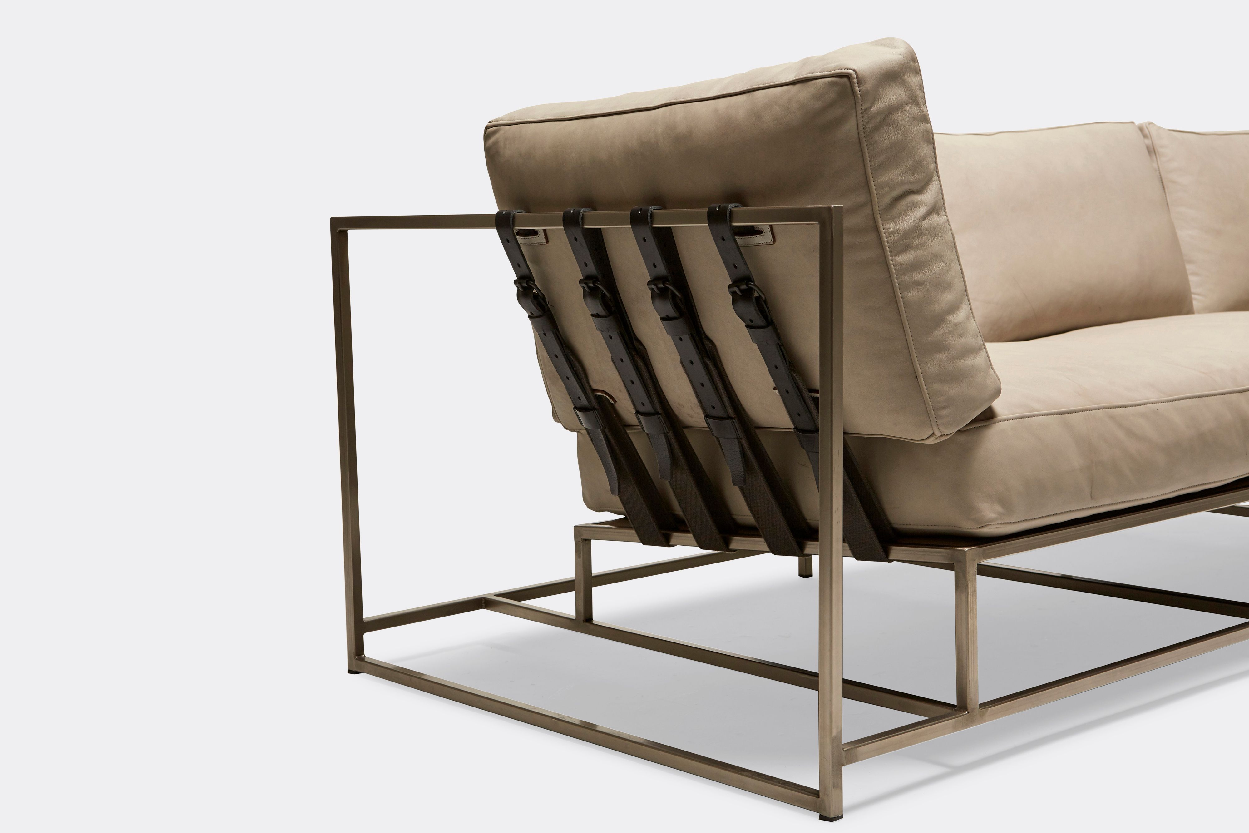 sideview of Sofa with cream leather upholstery and black leather belts on antique nickel metal frame