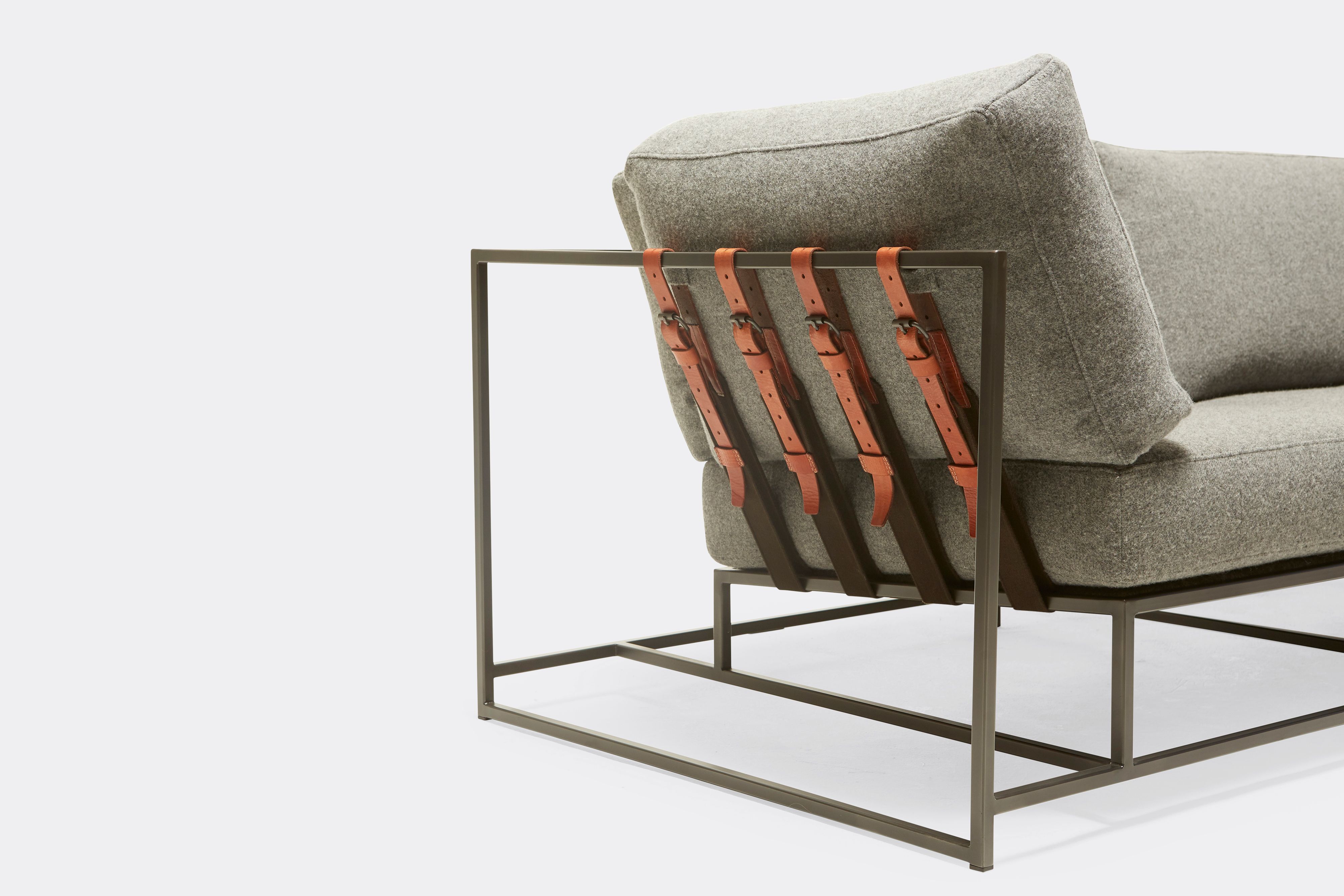 sideview of two seat sofa with grey wool upholstery and brown leather belts on black metal frame