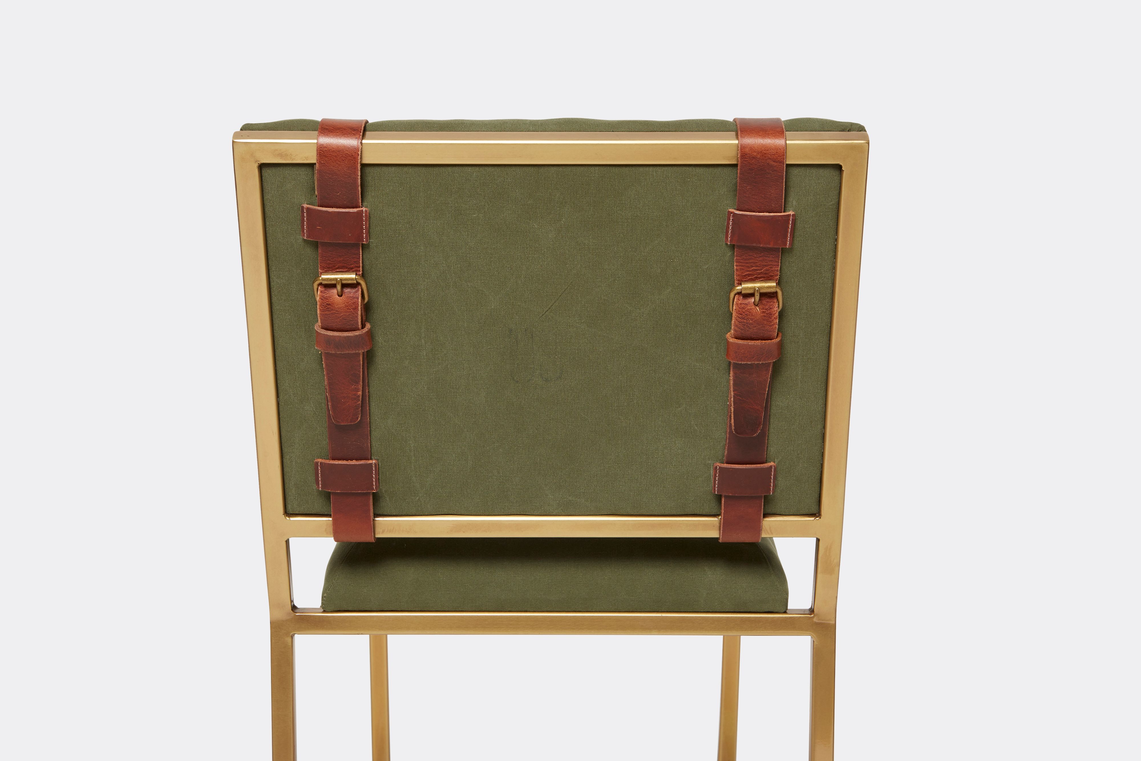 Detail of barstool with military canvas upholstery and brown leather belts on antique brass metal legs