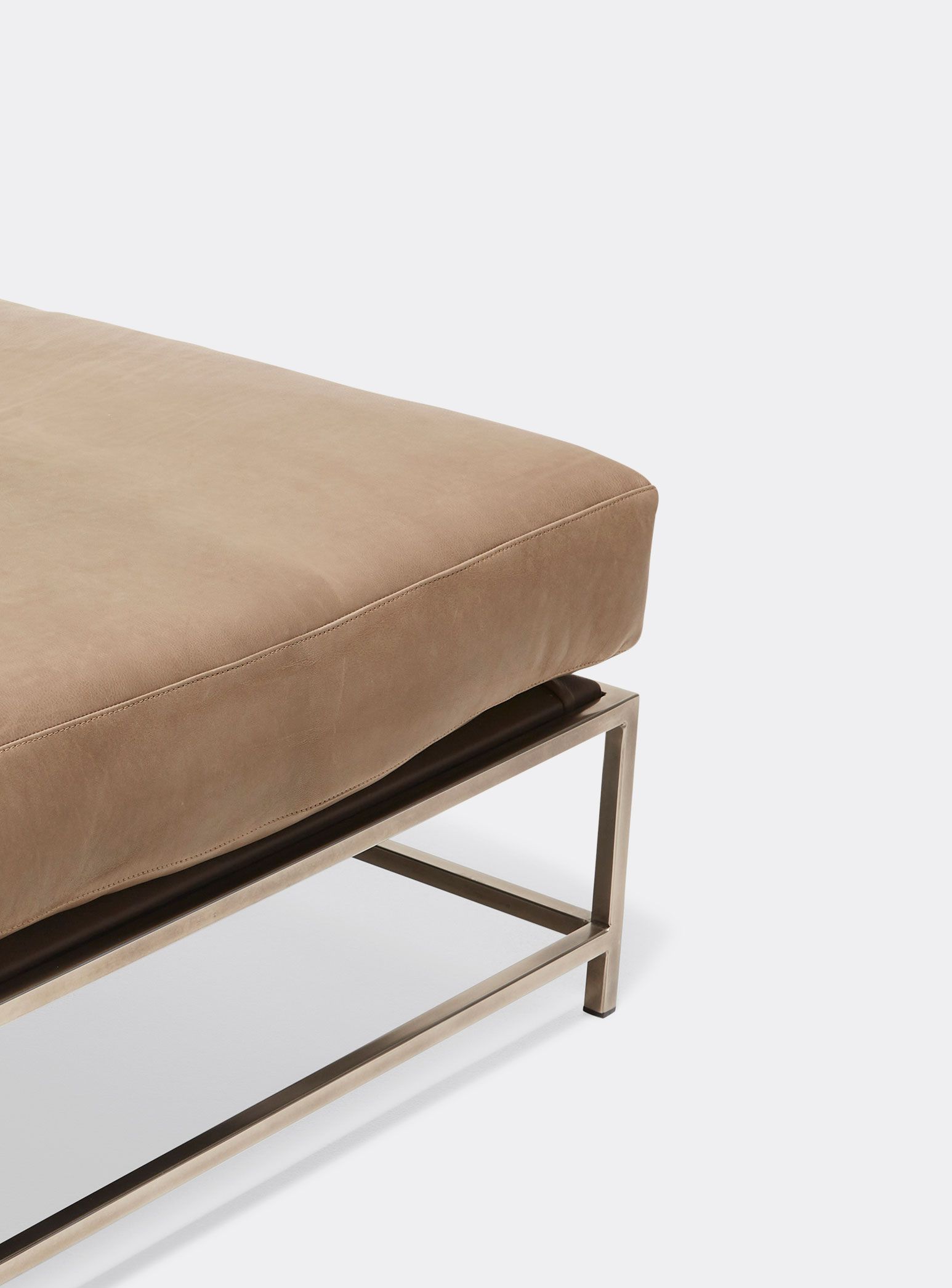 a tan leather ottoman with a metal frame shown on a white background .