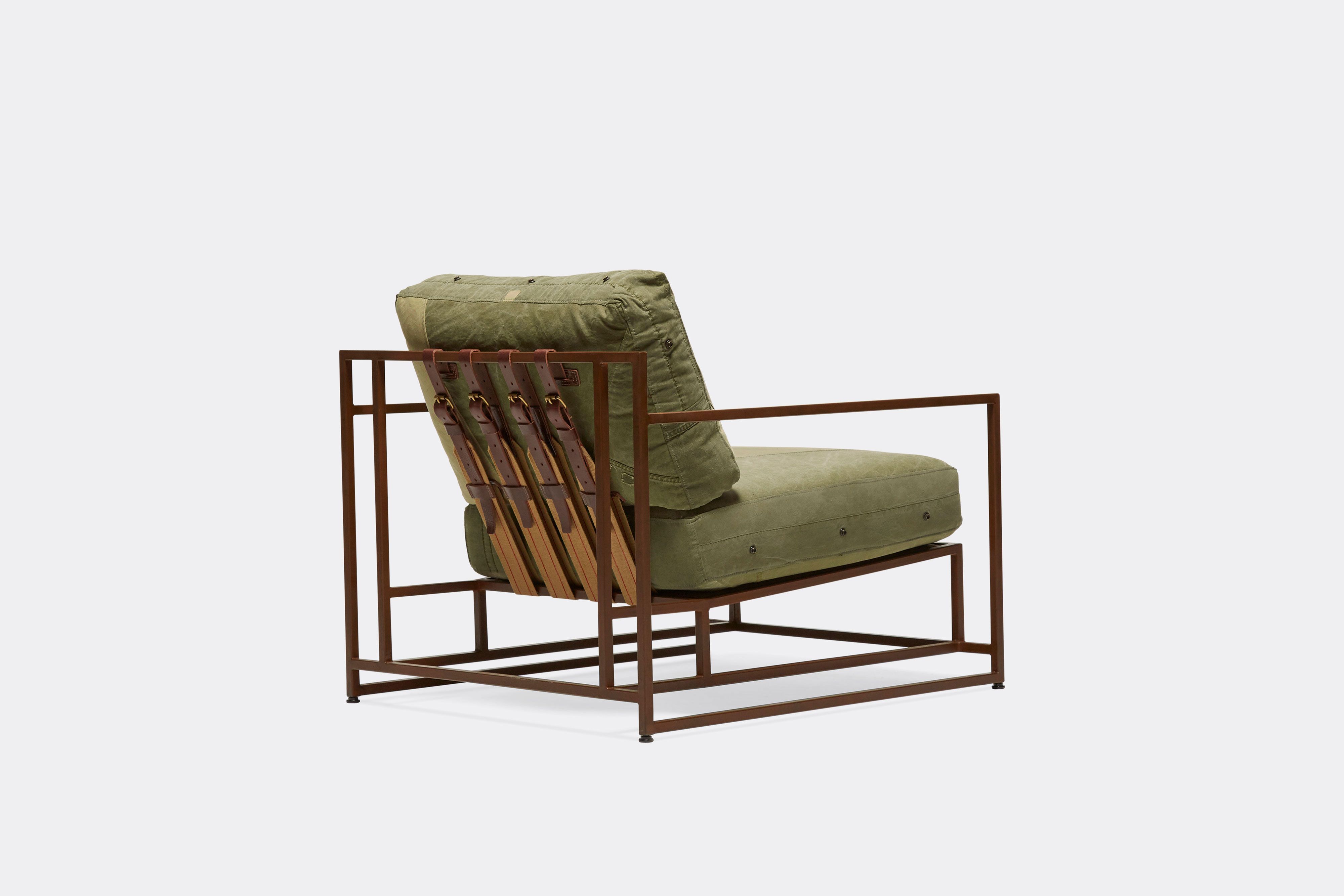 side of armchair with green canvas upholstery and brown leather belts on marbled rust metal frame