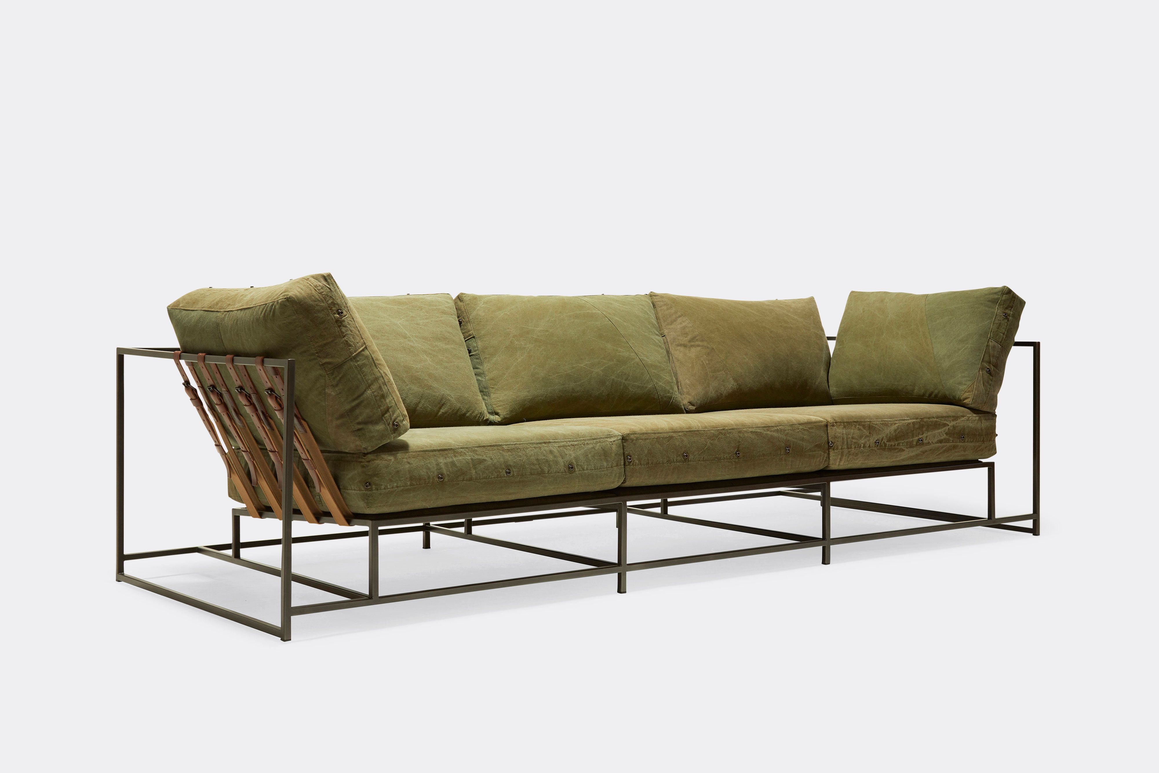 side of sofa with green canvas upholstery and brown belts on black metal frame
