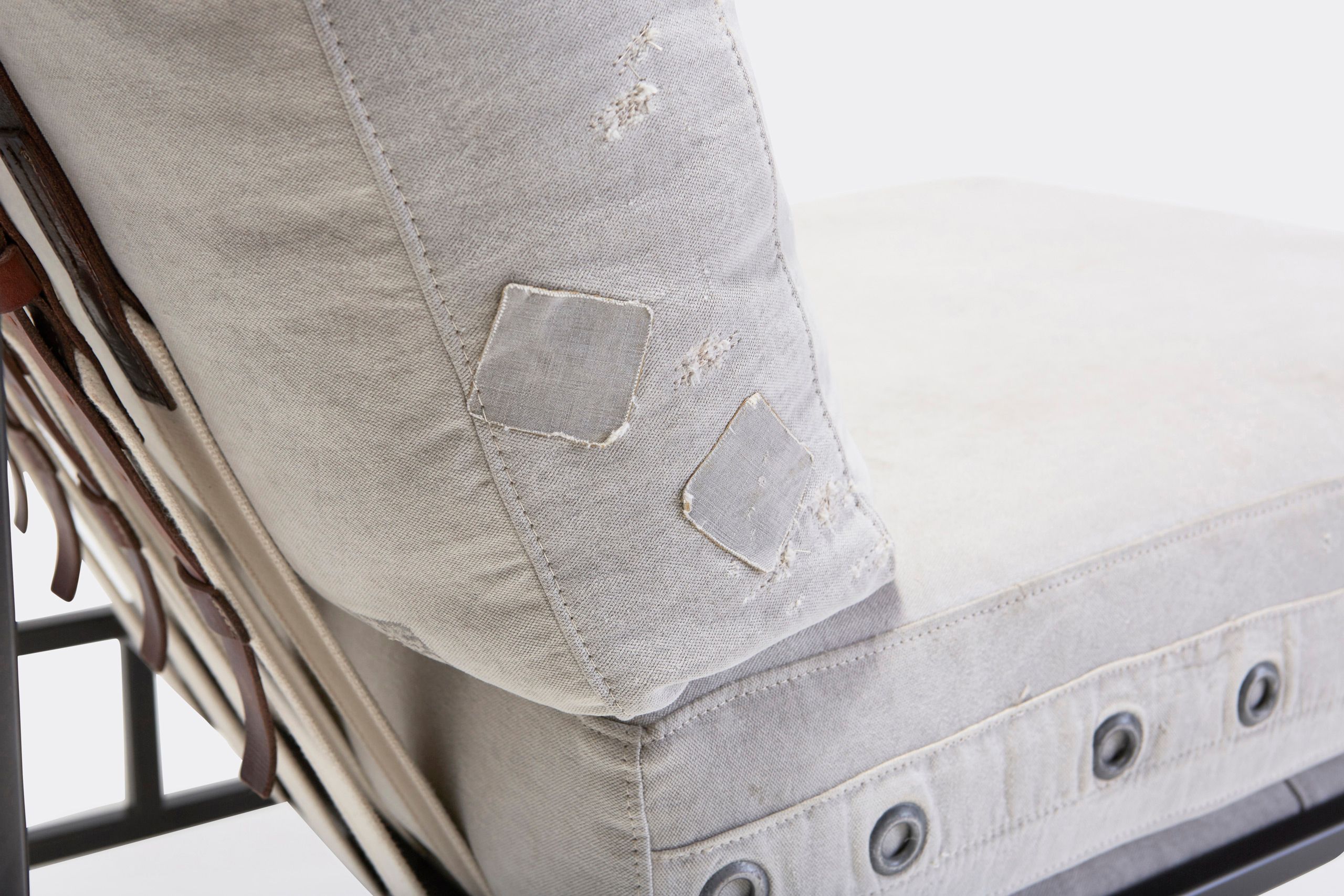 A chair with a white cushion and leather straps atop a blackened steel frame on a white background