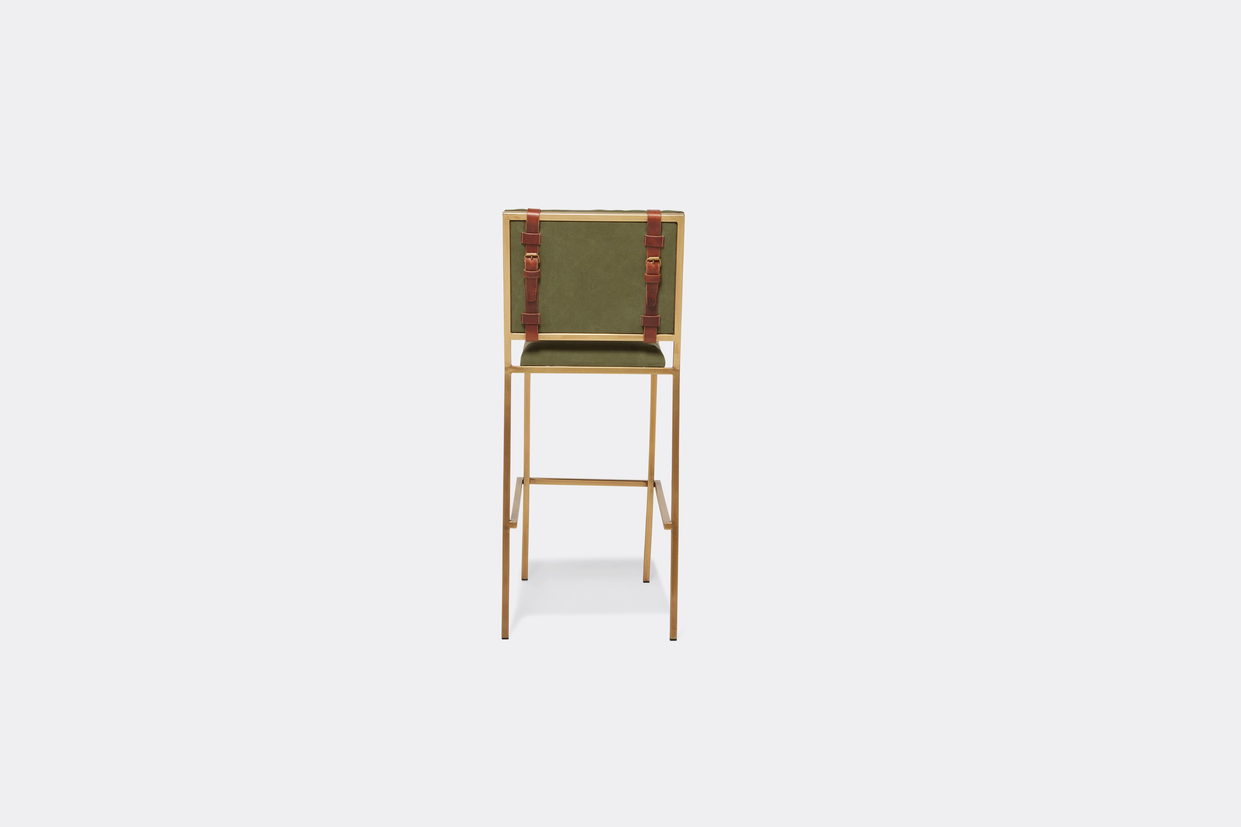 Back of barstool with military canvas upholstery and brown leather belts on antique brass metal legs