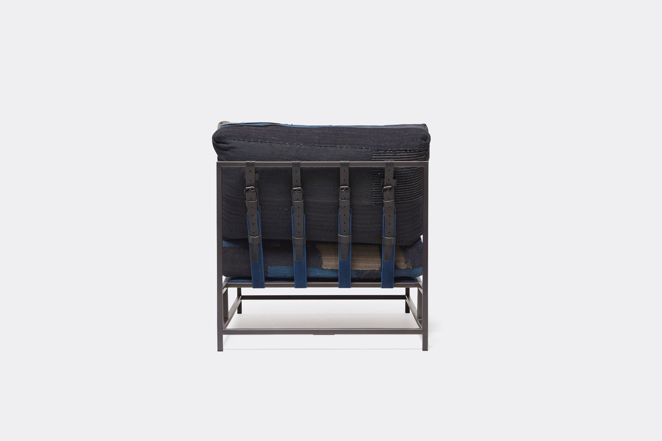 A steel framed chair upholstered with vintage japanese indigo and grey quilted material and blue and black supporting belts shown on a white background