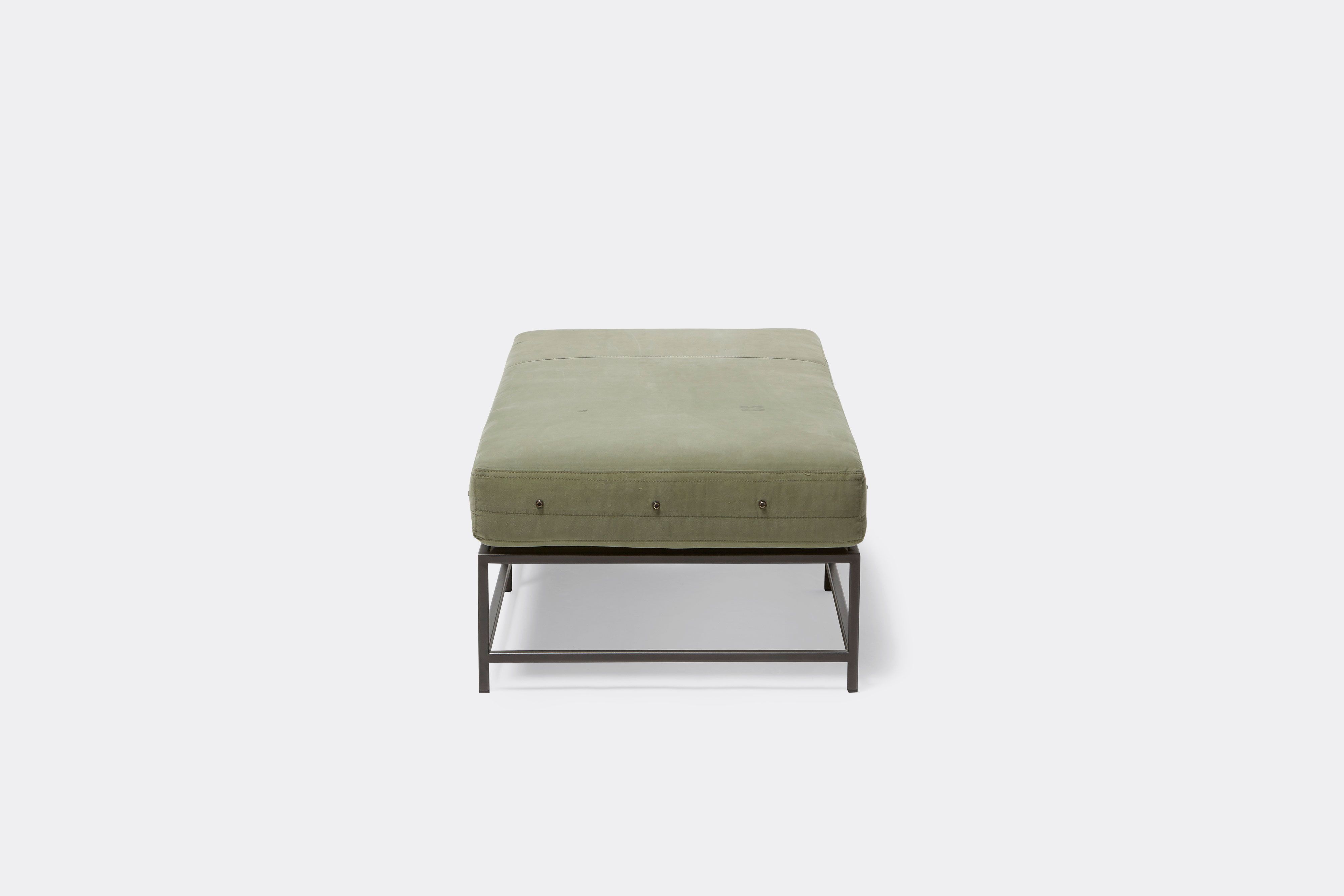 side of bench with green canvas upholstery on black metal frame.