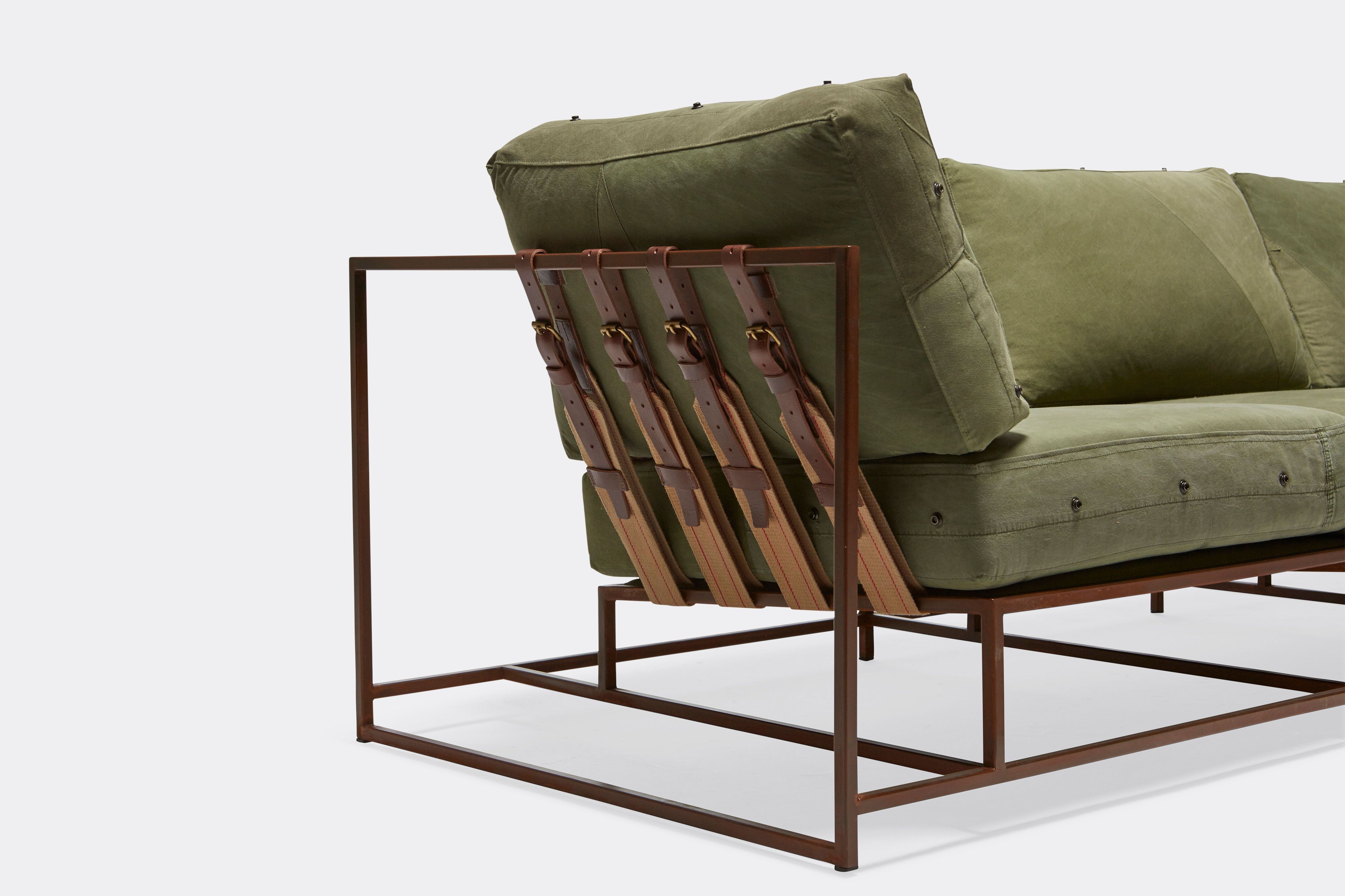 side detail of sofa with green canvas upholstery and brown belts on marbled rust metal frame