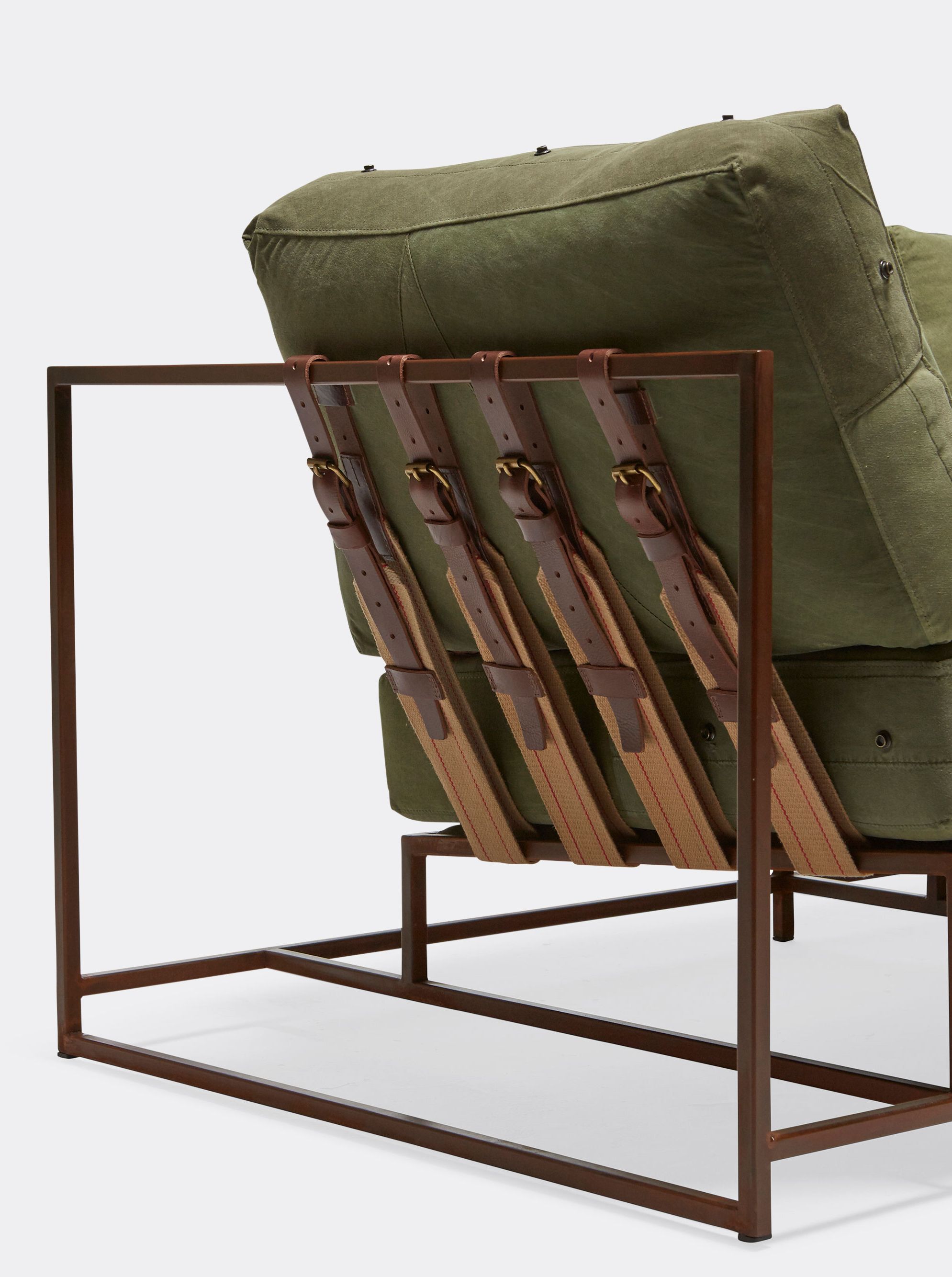 a green canvas upholstered sofa with a marbled rust steel frame and leather and webbing supporting belts is shown on a white background