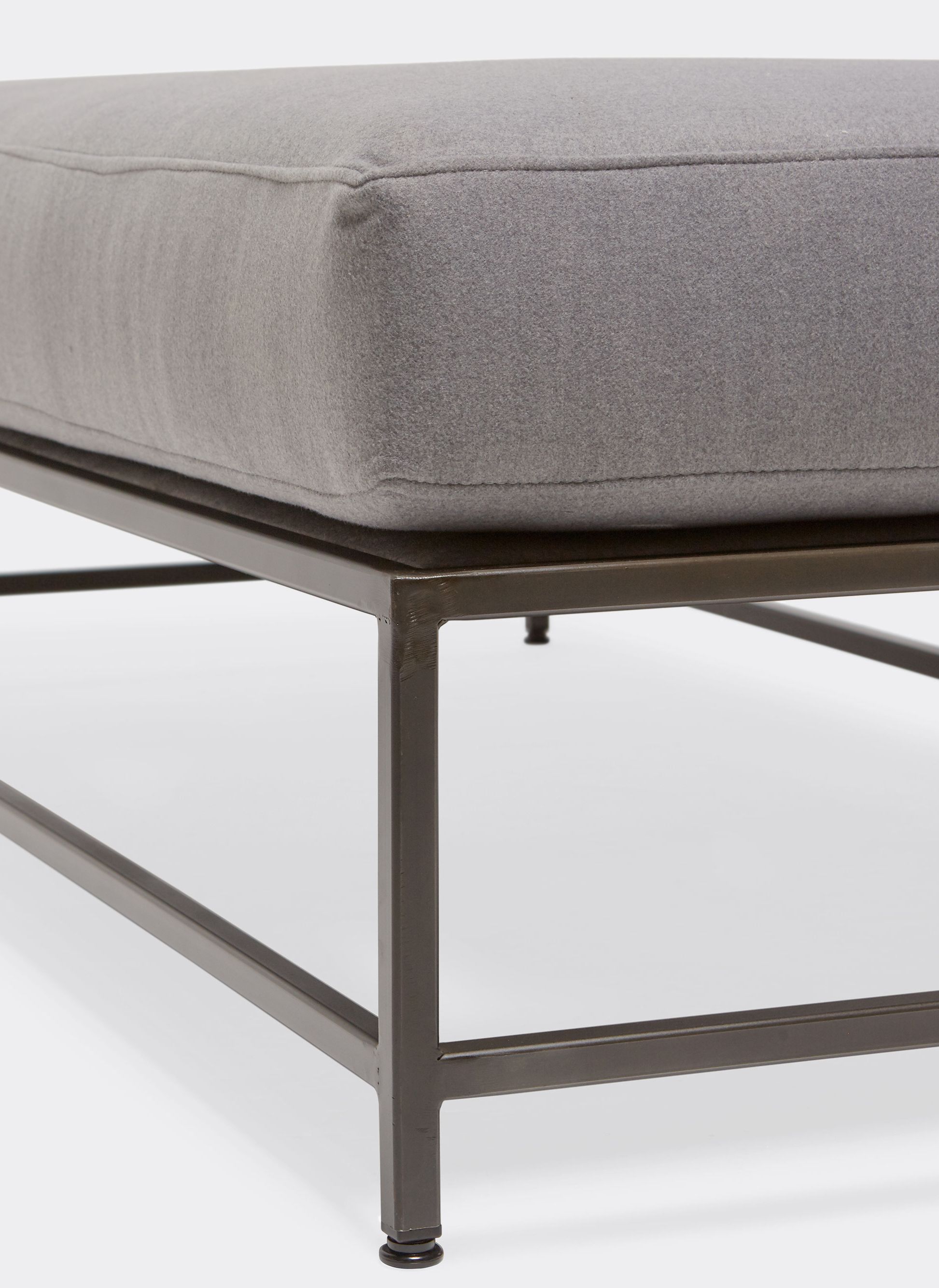 a gray wool upholstered bench with a metal frame shown on a white background .
