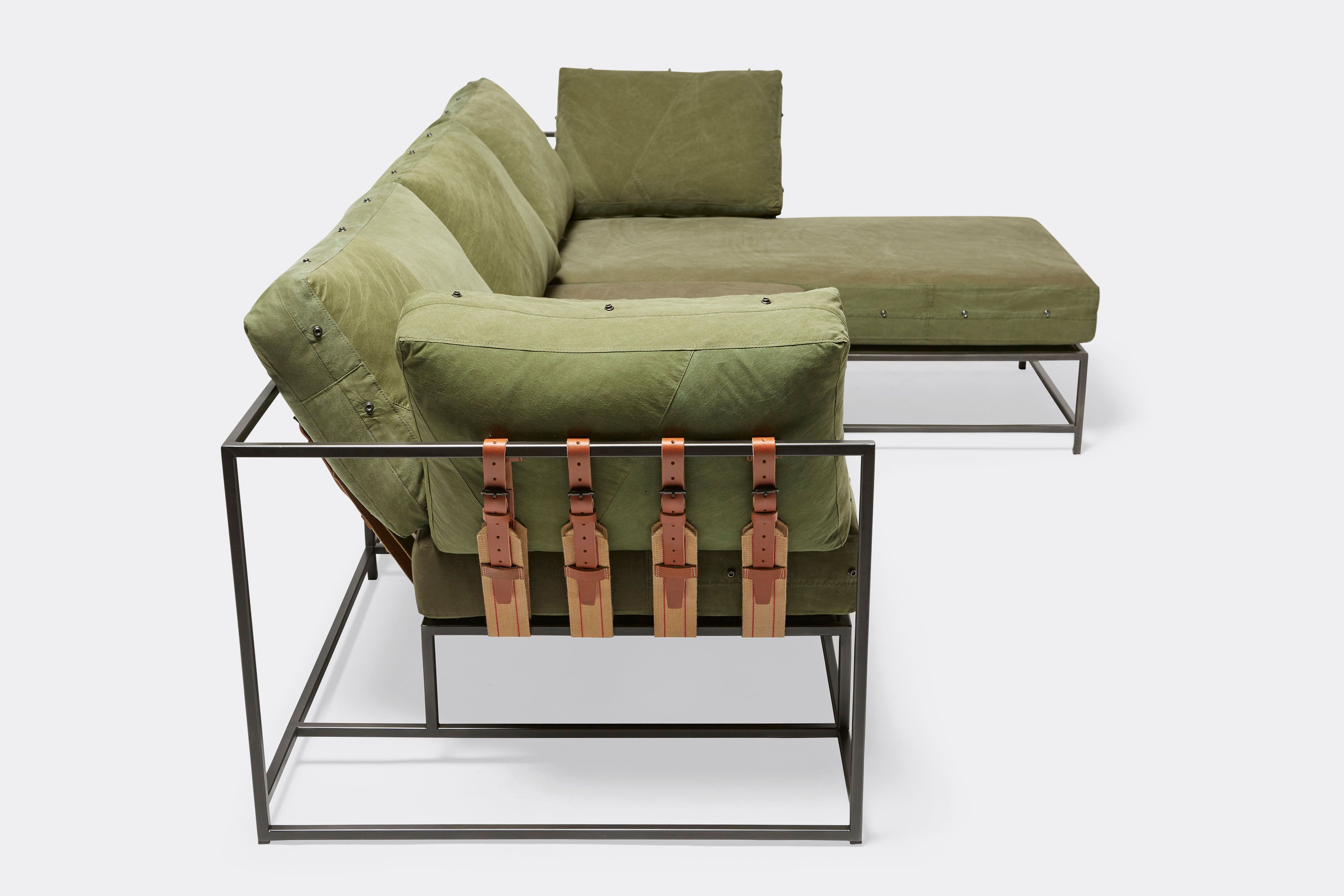 side of sectional with green canvas upholstery and brown leather belts on black metal frame