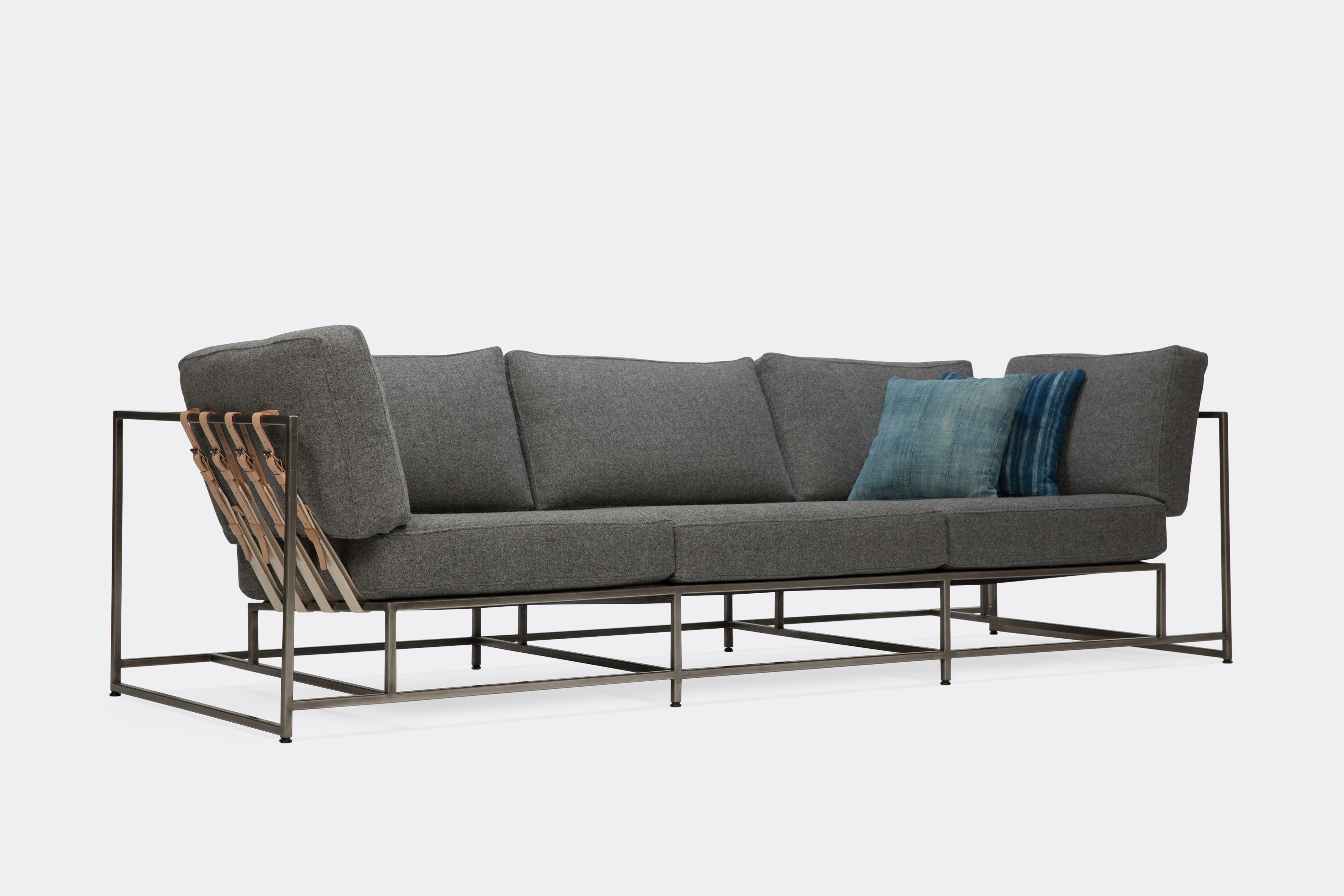 sideview of sofa with grey wool upholstery and veg tan leather belts on antique nickel metal frame