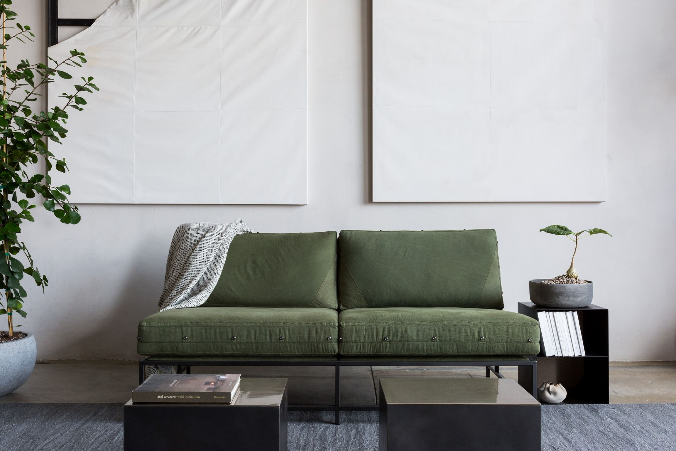 a living room with a green couch and two coffee tables and a potted tree with white canvas art on the wall