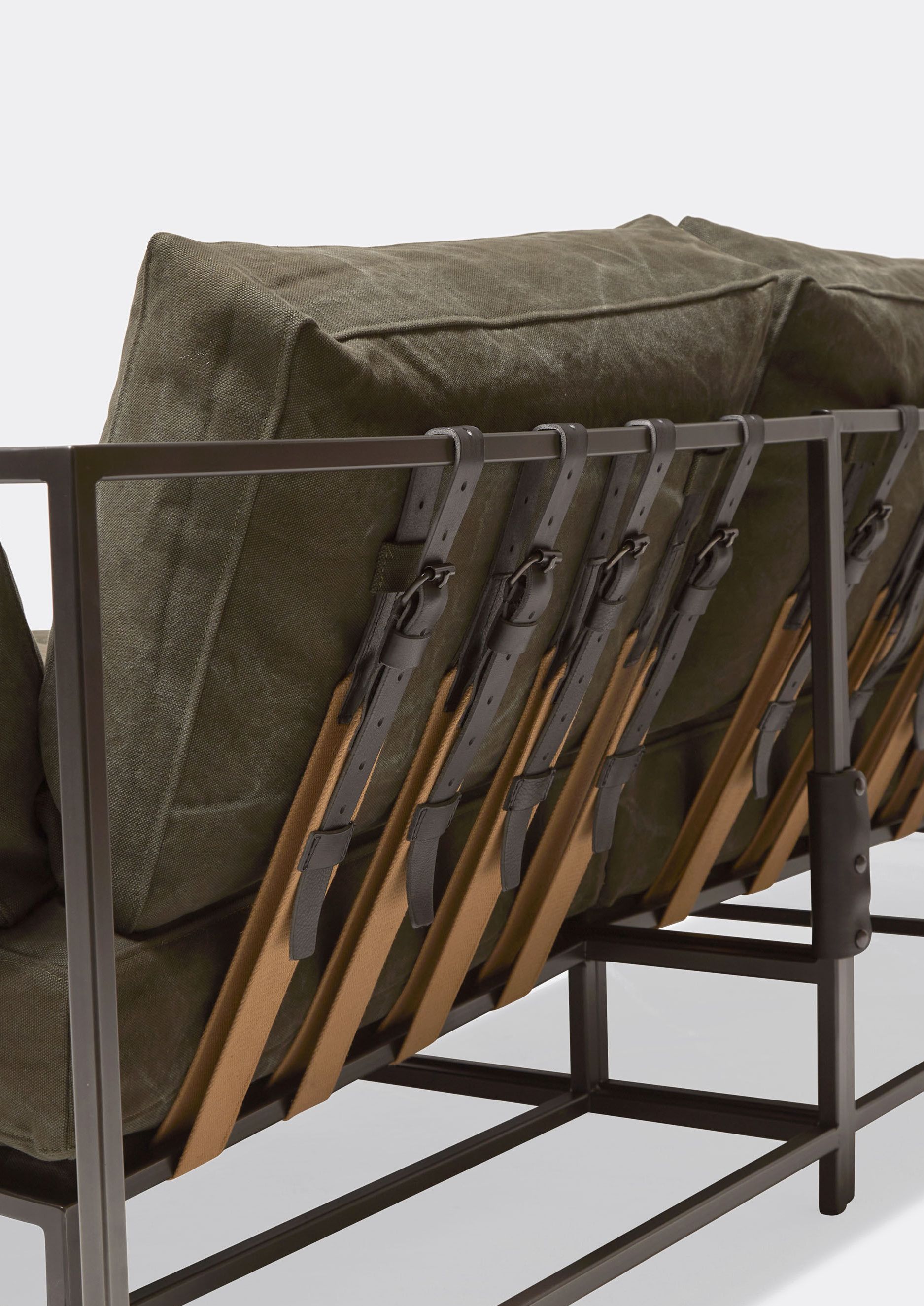 A sofa with a metal frame and olive green canvas cushions with supporting belts  shown on a white background .