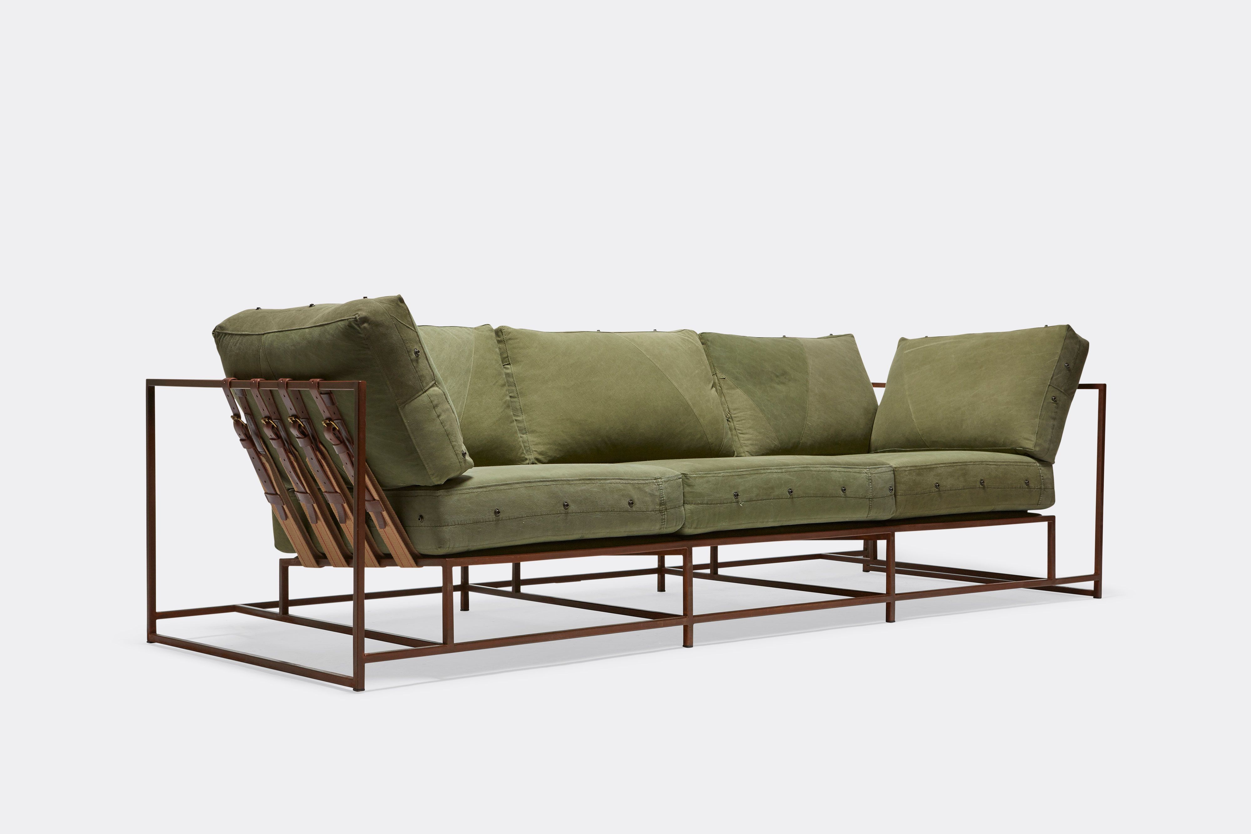 side of sofa with green canvas upholstery and brown belts on marbled rust metal frame