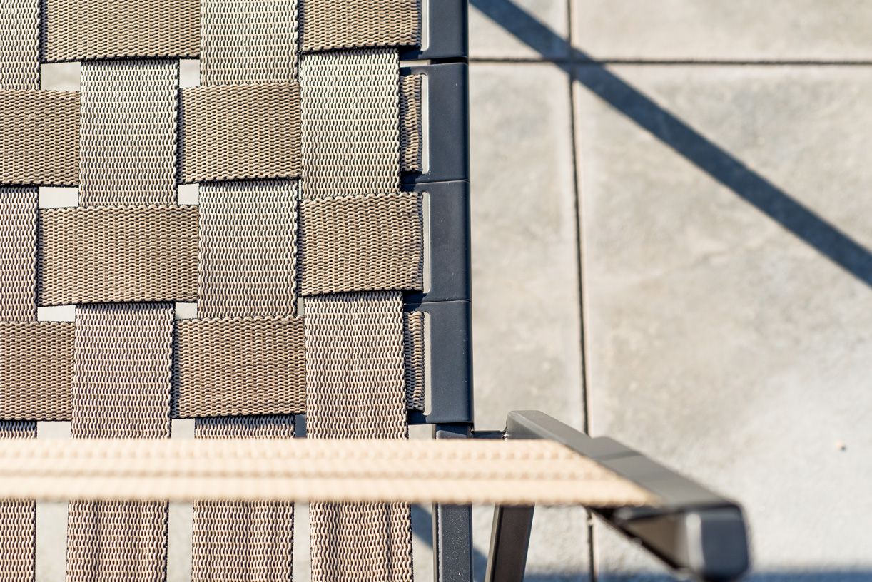 An outdoor steel chair with black metal finish and interwoven tan webbing on a light background