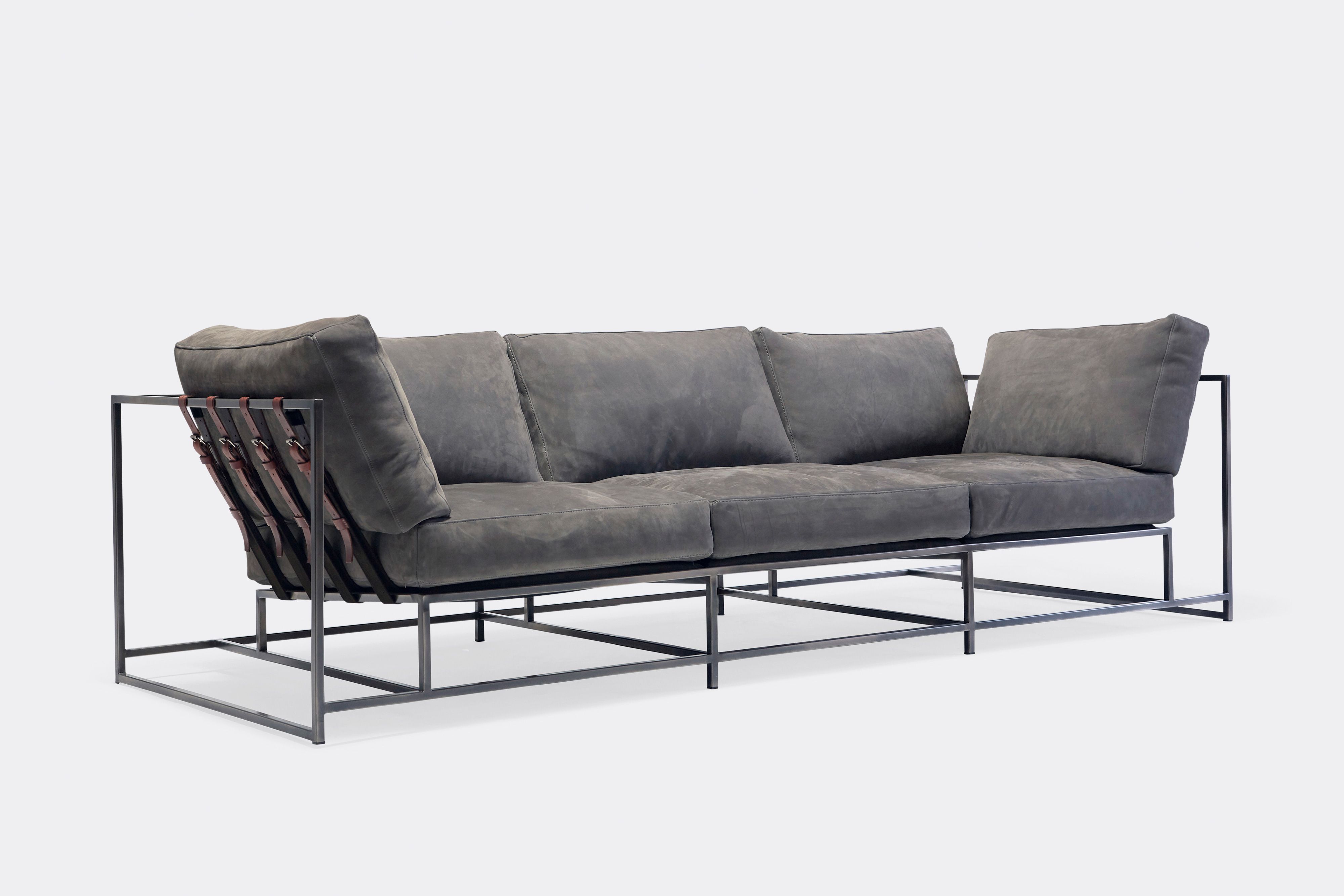 Sideview of sofa with grey leather upholstery and brown leather belts on antique nickel metal frame