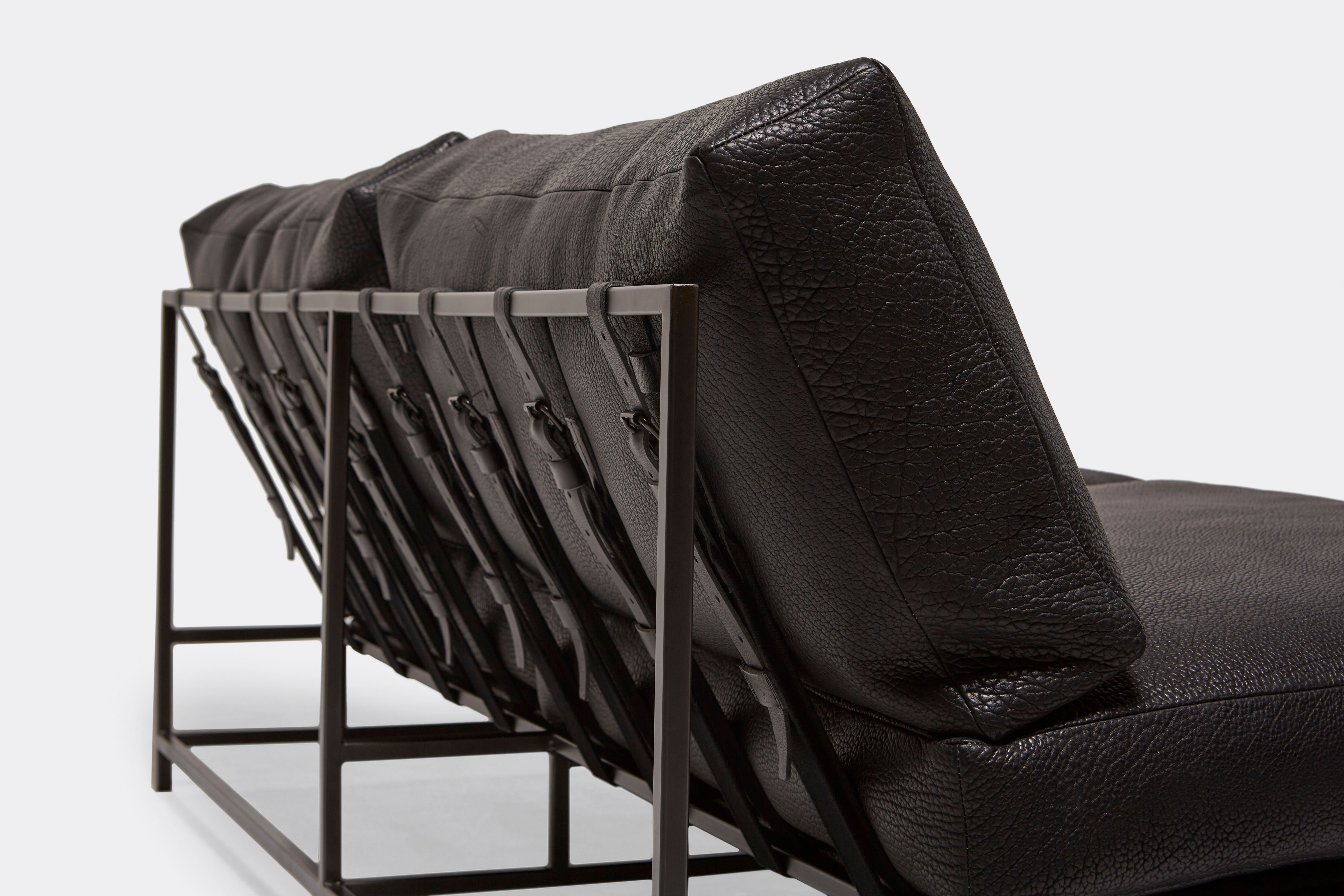 detail of loveseat with black leather upholstery and black leather belts on black metal frame