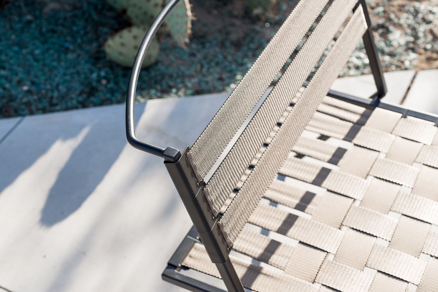An outdoor steel chair with black metal finish and interwoven tan webbing on a light background