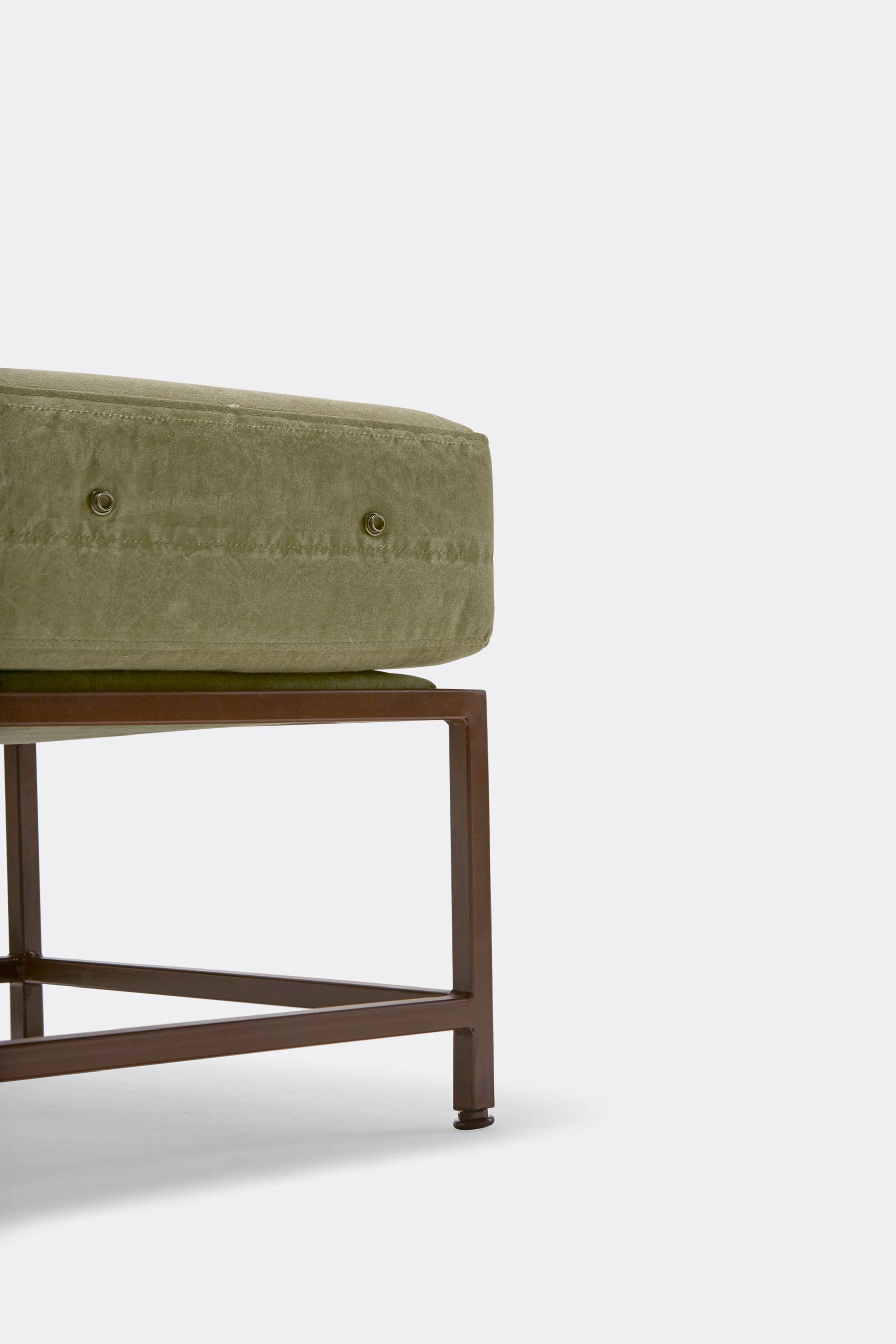 an ottoman with a green cushion and a rust finished steel frame .
