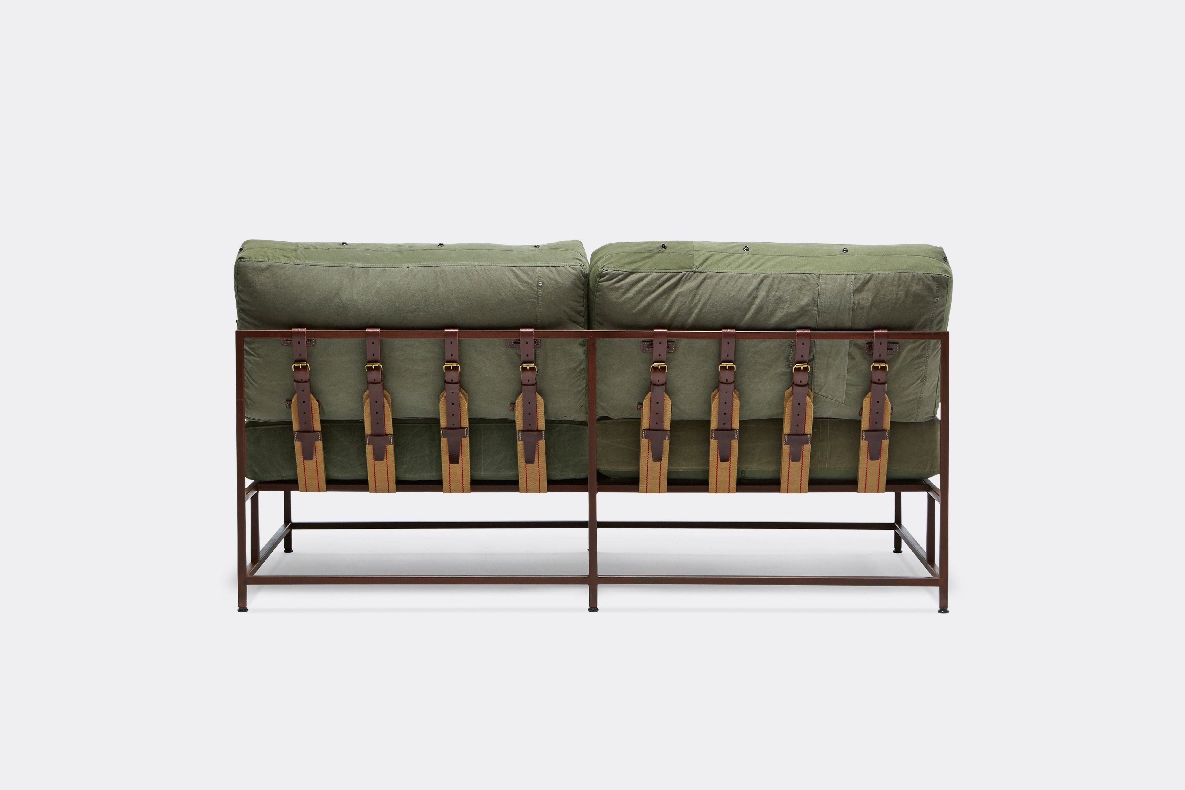 a steel framed loveseat sofa with green canvas cushions and leather and webbing supporting belts shown on a white background .