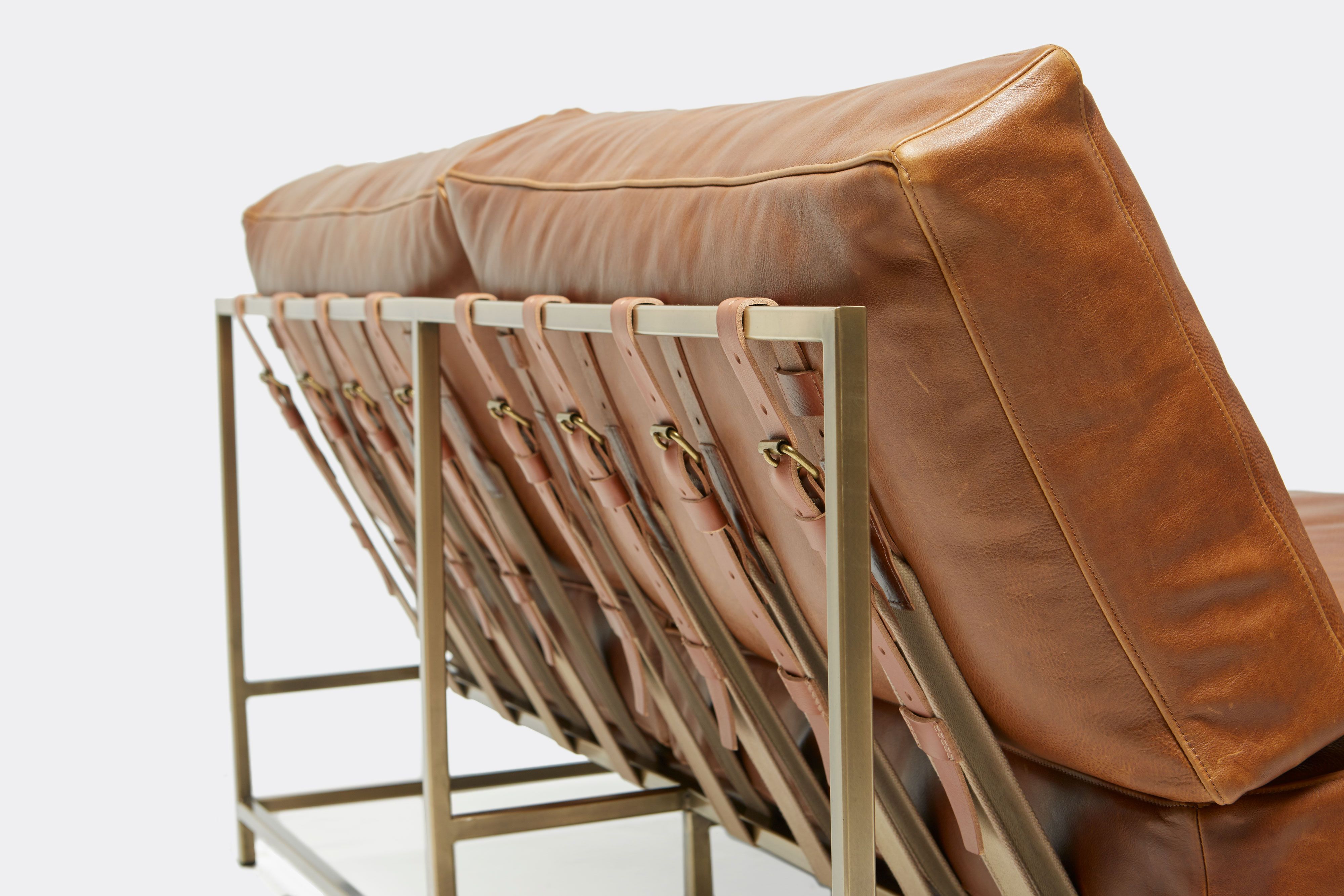 detail of loveseat with brown leather upholstery and brown leather belts on antique brass metal frame